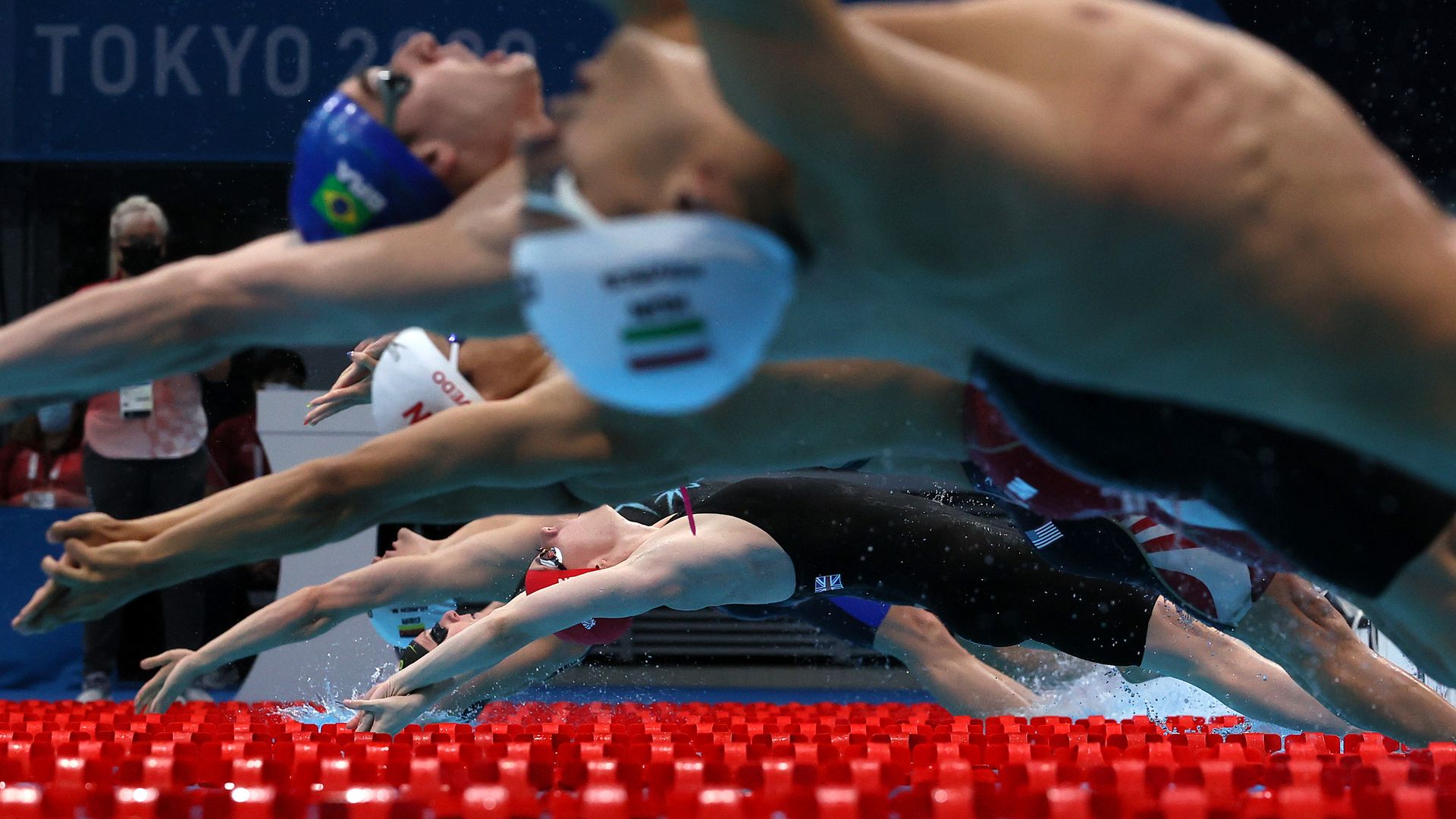 Photo of a row of swimmers diving backwards into the water at an Olympic pool
