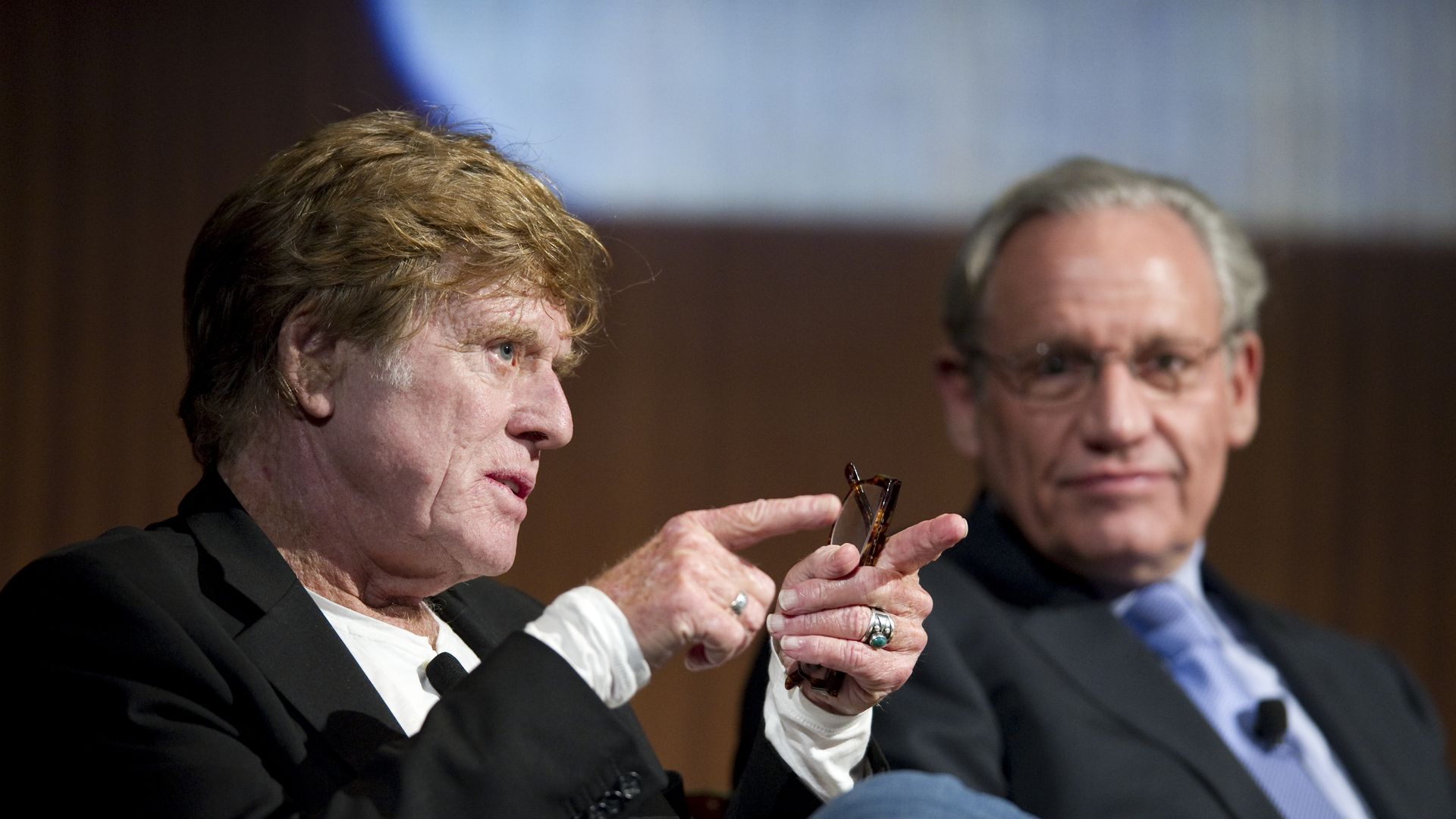 Robert Redford points while making a point. Bob Woodward is in the background.