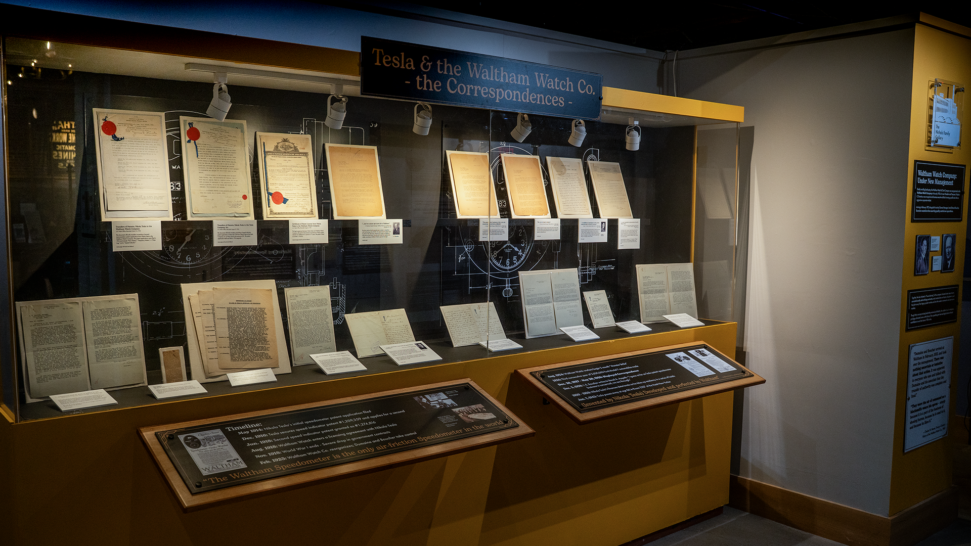 A series of letters and patent documents enclosed in a glass case with the words above that say, "Tesla & the Waltham Watch Co. the Correspondences." The display is at the Charles River Museum of Industry and Innovation in Waltham, Massachusetts