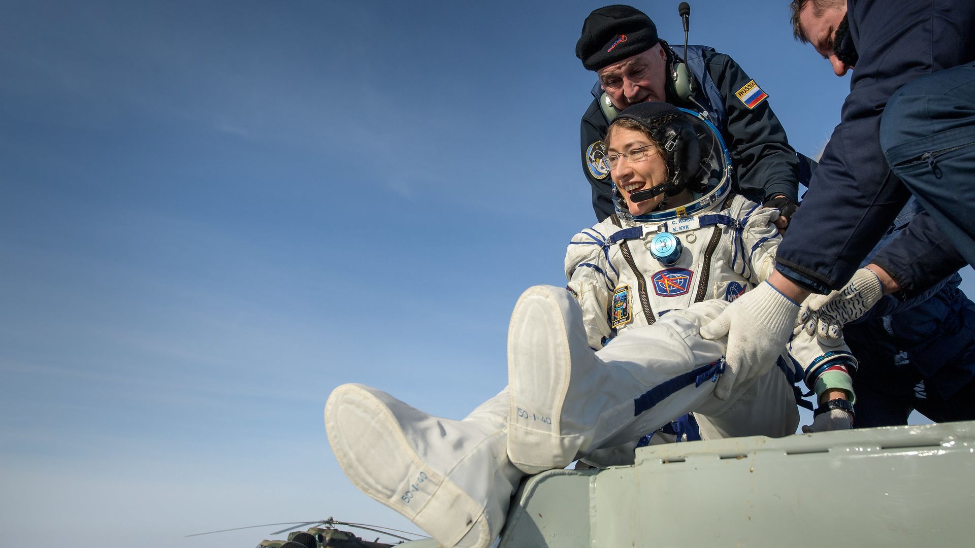 NASA astronaut Christina Koch smiles as she's pulled from her space capsule in Kazakhstan under a blue sky.