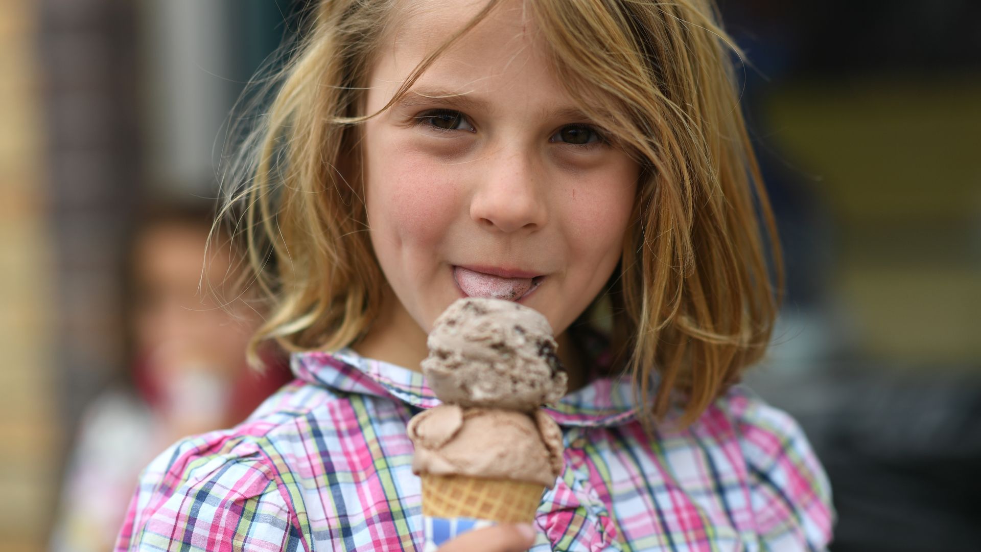 A young girl tases an cone with two ice cream scoops on it. 