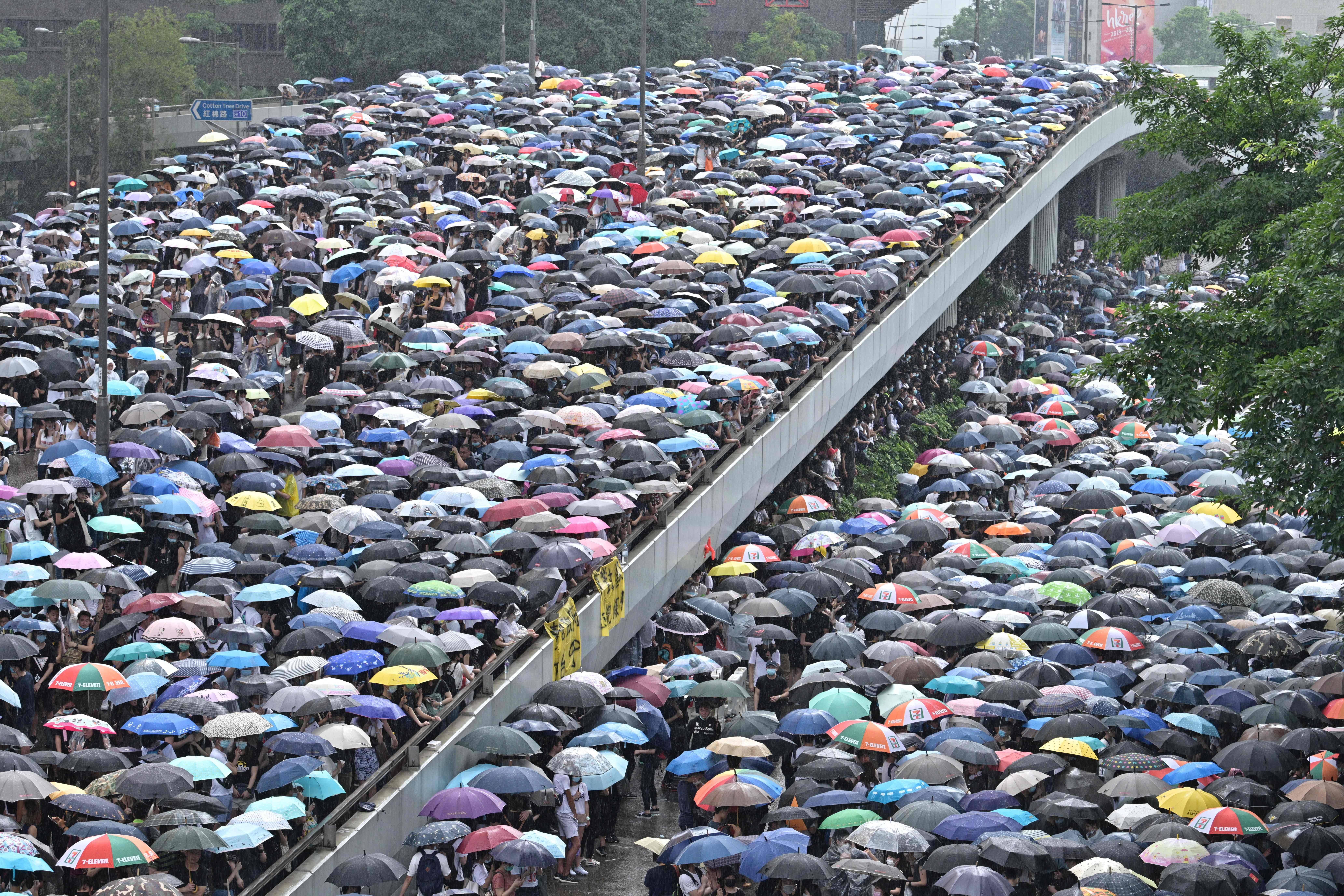 Protesters shelter under umbrellas during a downpour as they occupy roads near the government headquarters in Hong Kong on June 12, 2019. - Tens of thousands of protesters paralysed central Hong Kong.