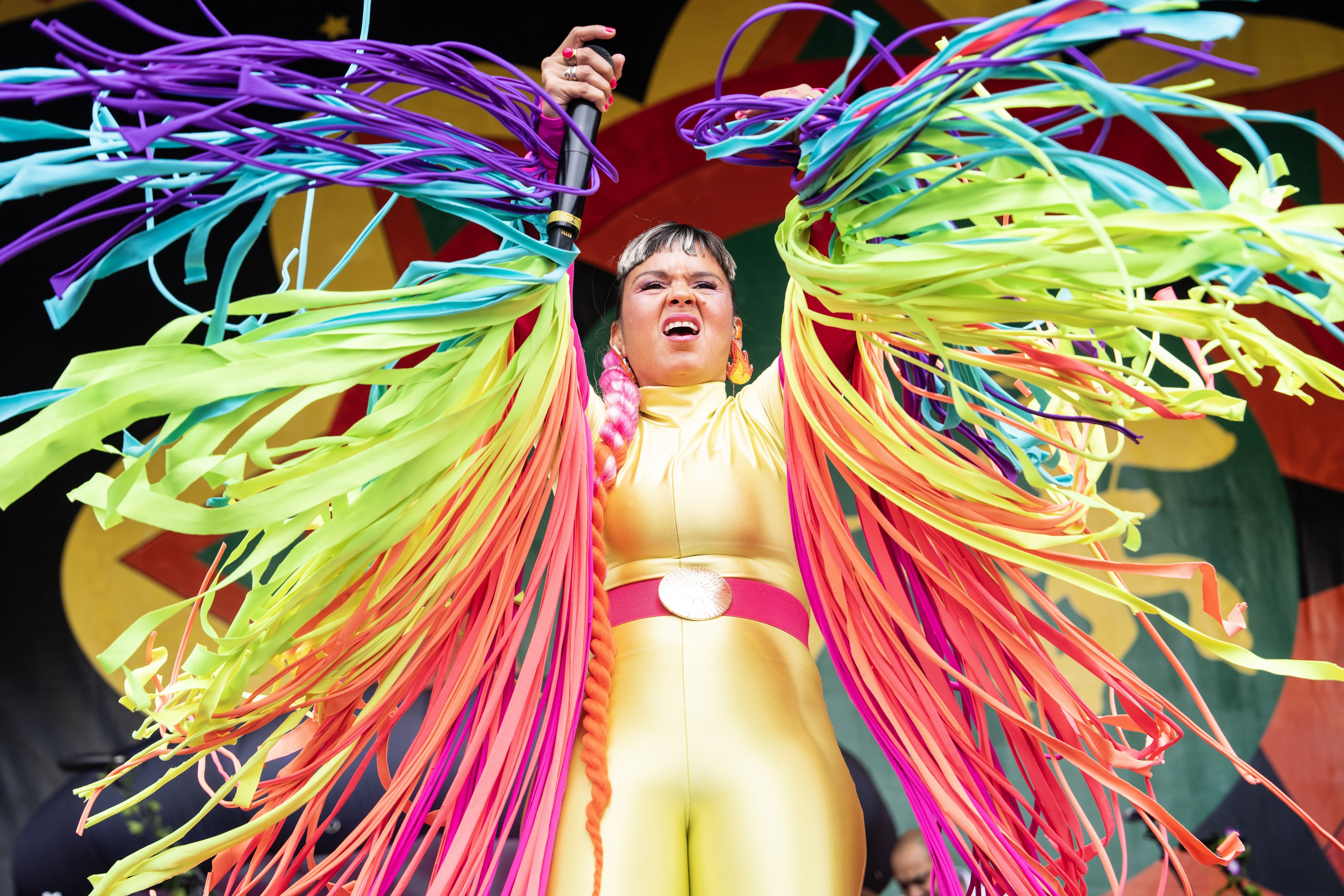 Liliana "Li" Saumet of Bomba Estereo gestures into the air while wearing rainbow-colored streamers on her arms.