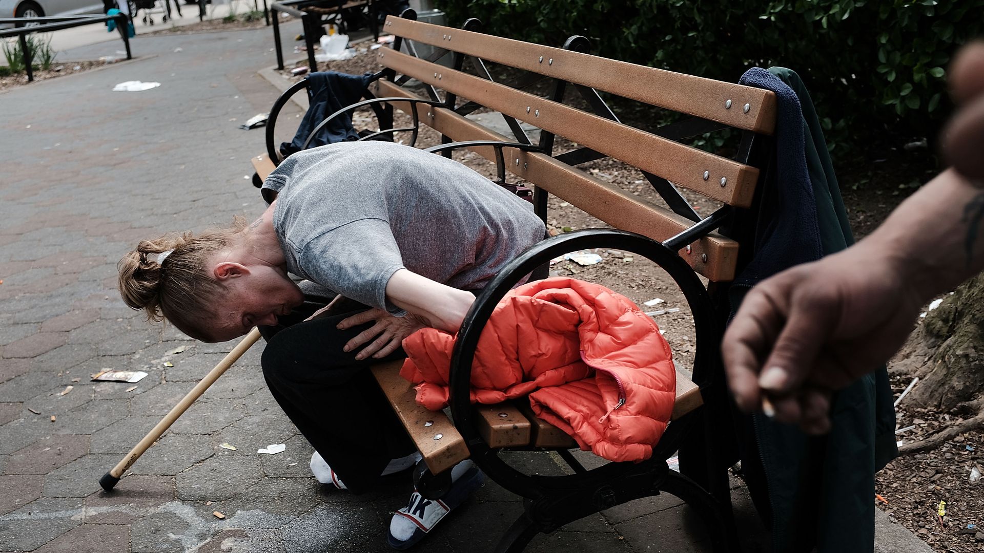 In this image, a woman leans over her knees while sitting on a park bench.