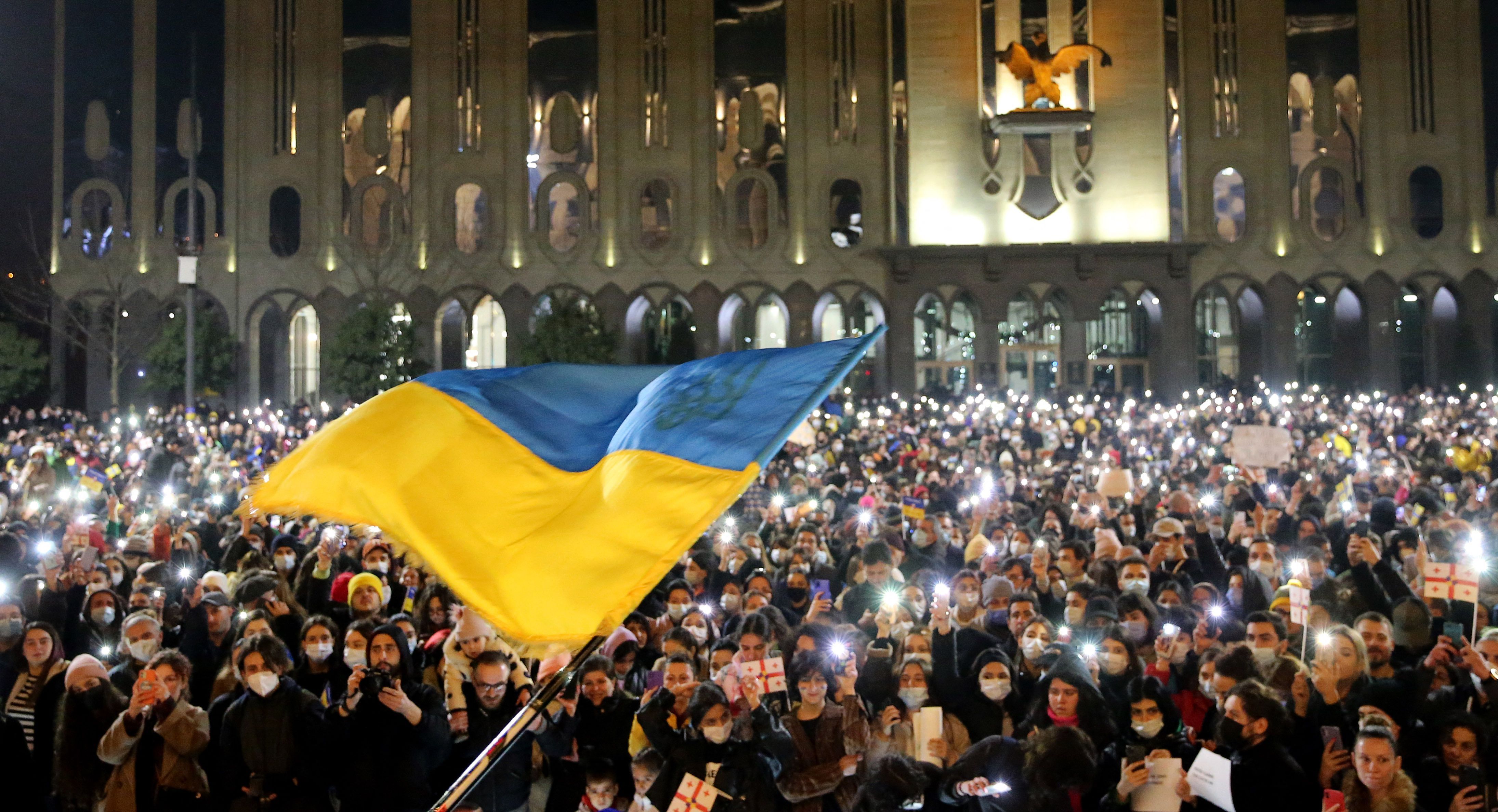 Photo of a large Ukraine flag being waved in the air in front of a crowd of people holding lights