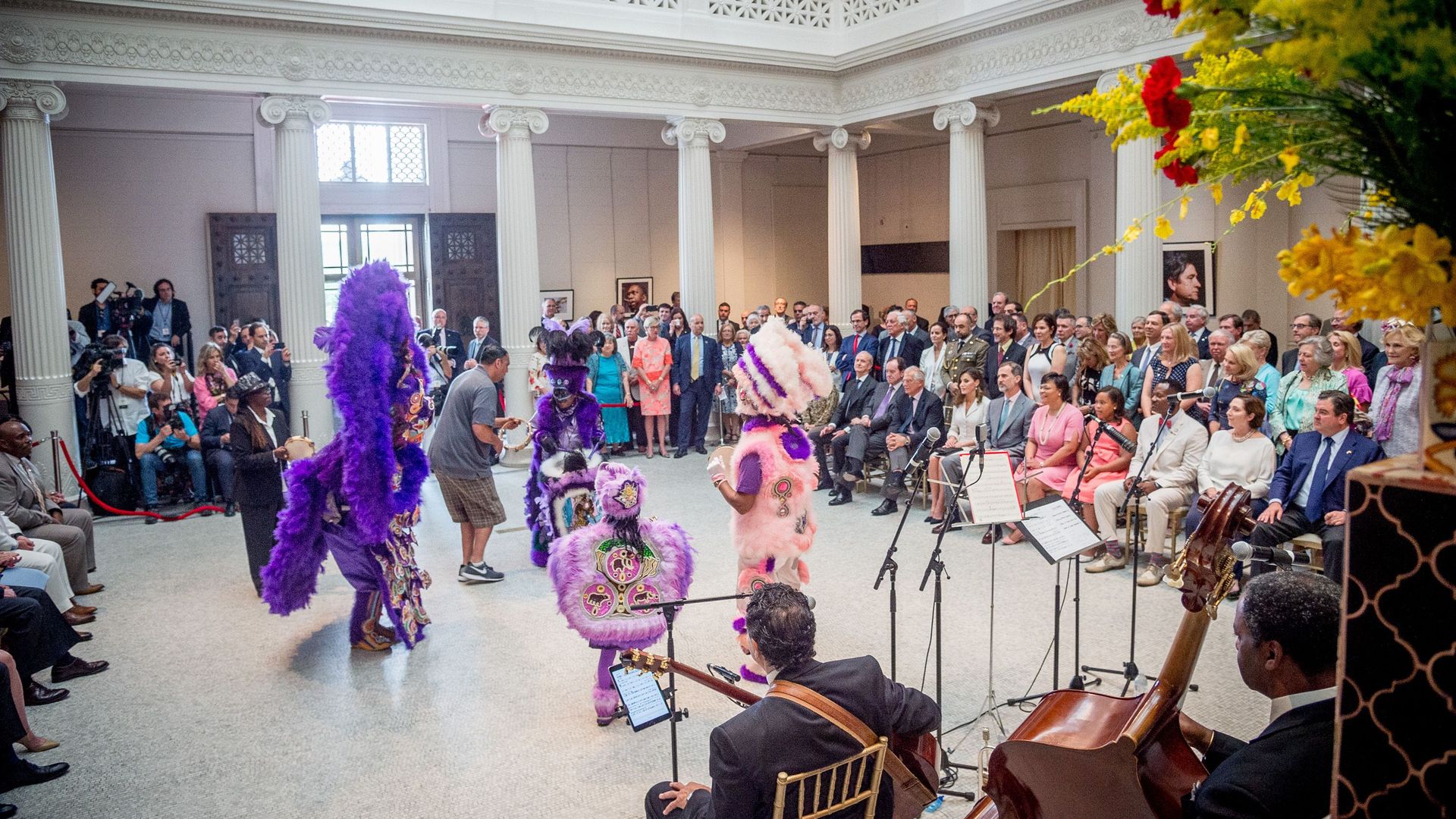 Photo shows a brass band and Mardi Gras Indians performing inside the New Orleans Museum of Art