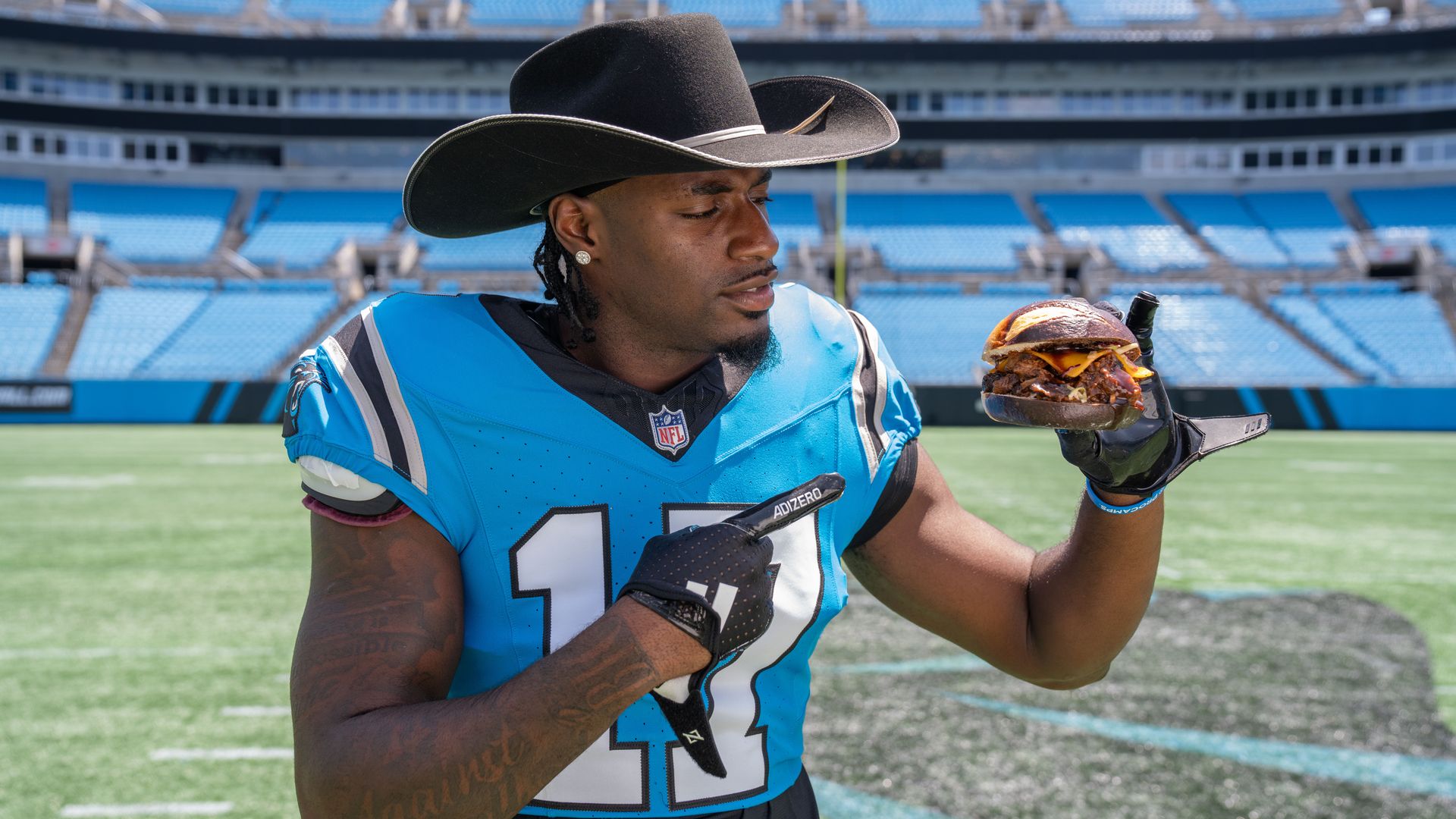 Carolina Panthers wide receiver Xavier Legette on the field at Bank of America Stadium holding and pointing to a sandwich. 