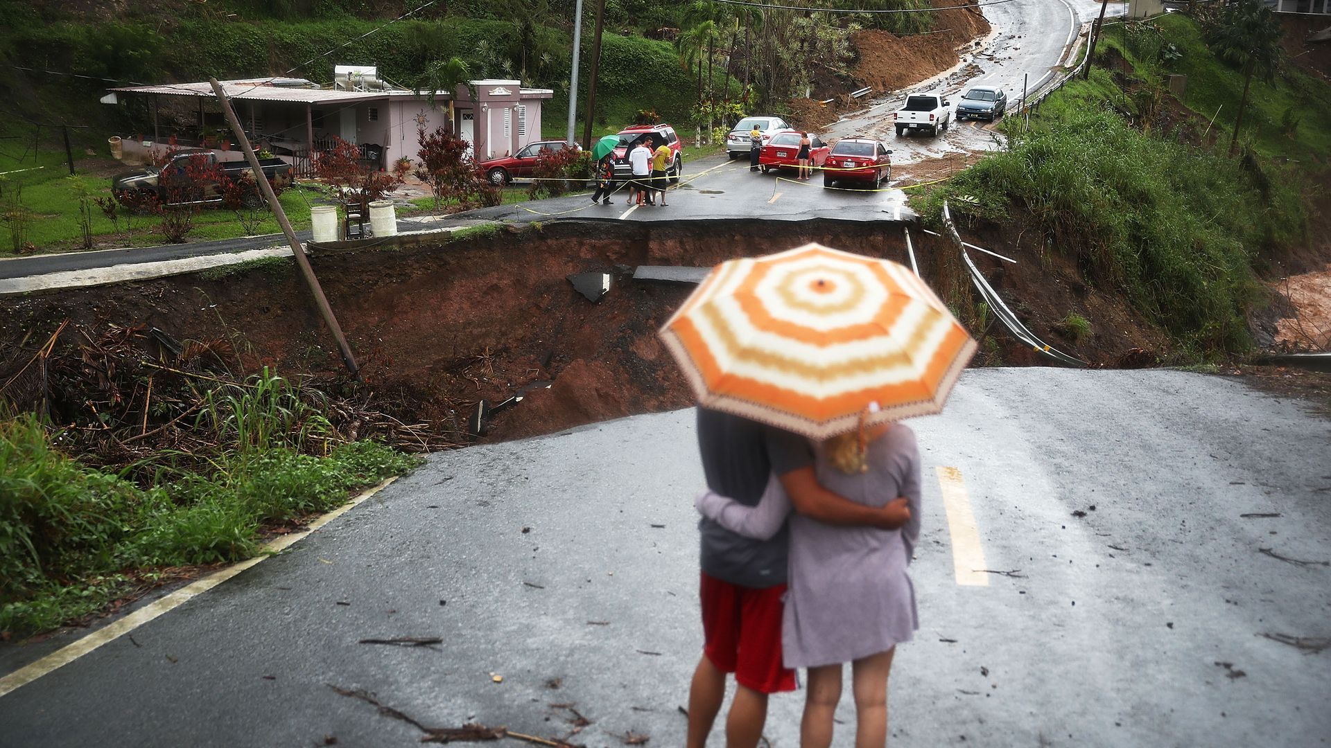 People look on at a section of a road that collapsed in Barranquitas, Puerto Rico after Hurricane Maria swept through the island in 2017.