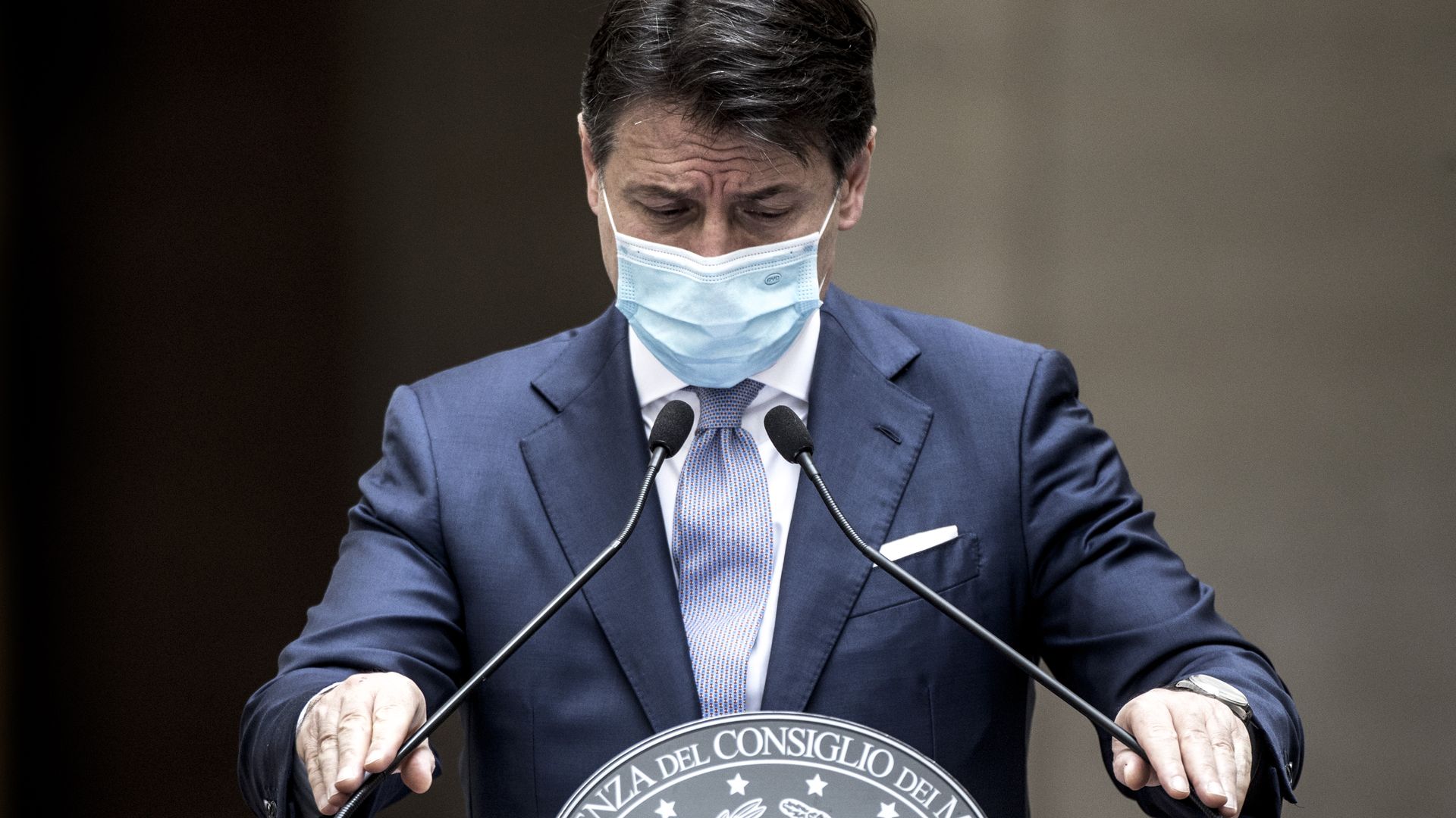 Italy's prime minister leans on a podium while wearing a face mask
