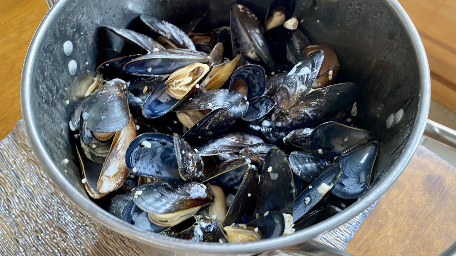 A stainless steel pot filled with steamed mussels on a wooden table.