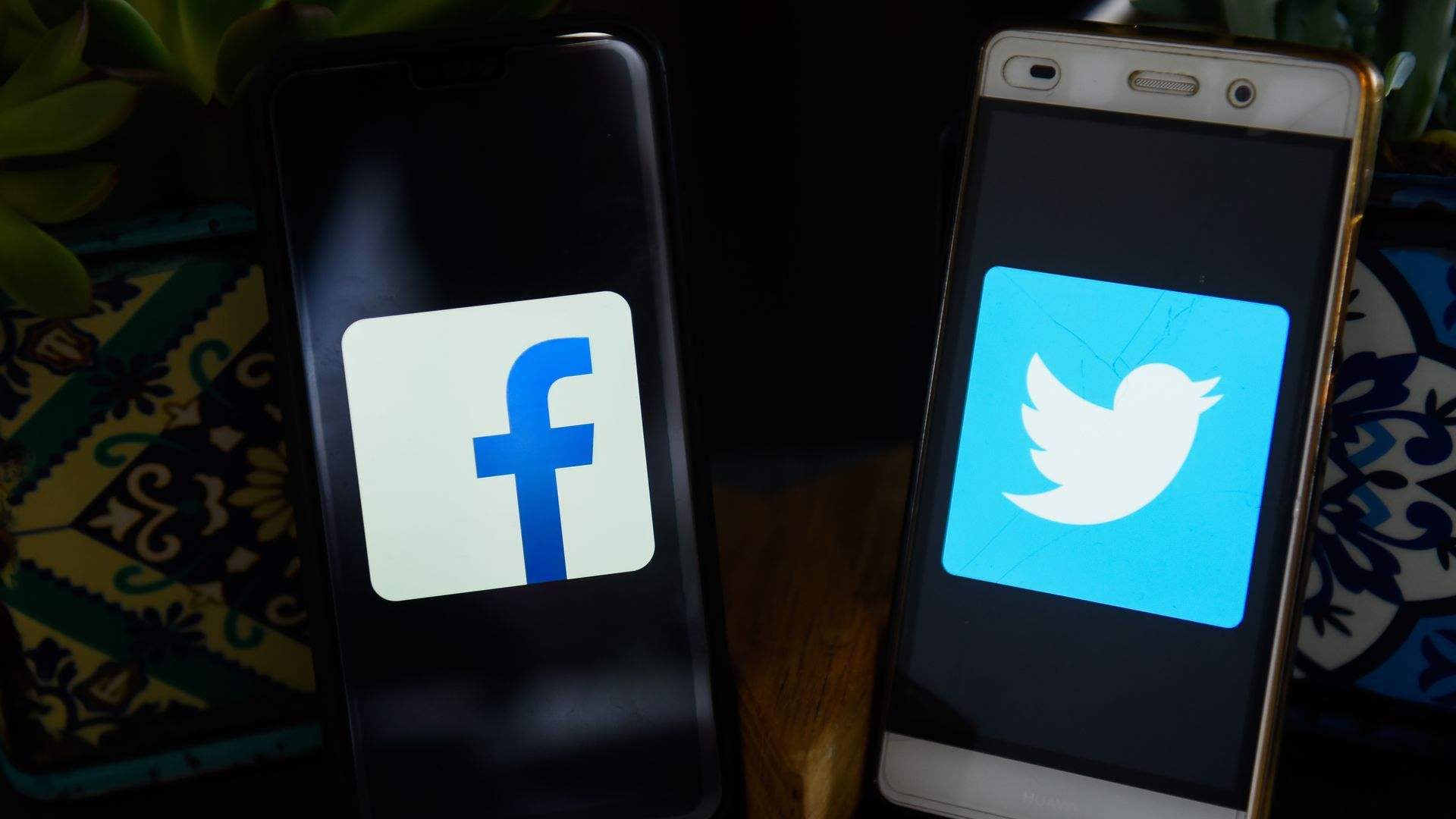 Two smartphones show the logos for Facebook and Twitter on their respective screens.