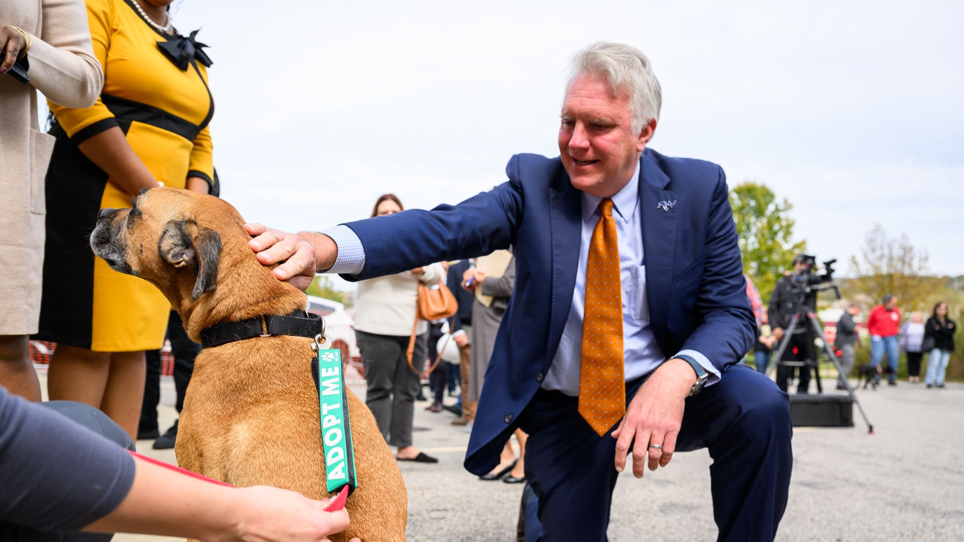 A man in blue suit pets a dog with an "adopt me" pennant around its neck