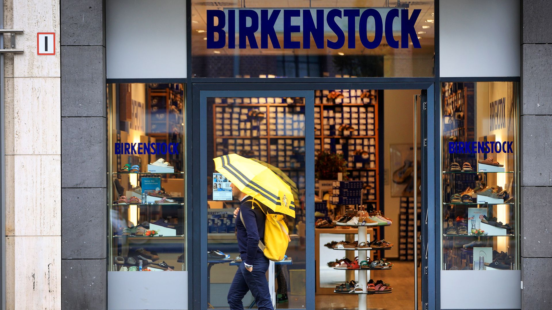 A person with an umbrella walks past the front of a Birkenstock store.