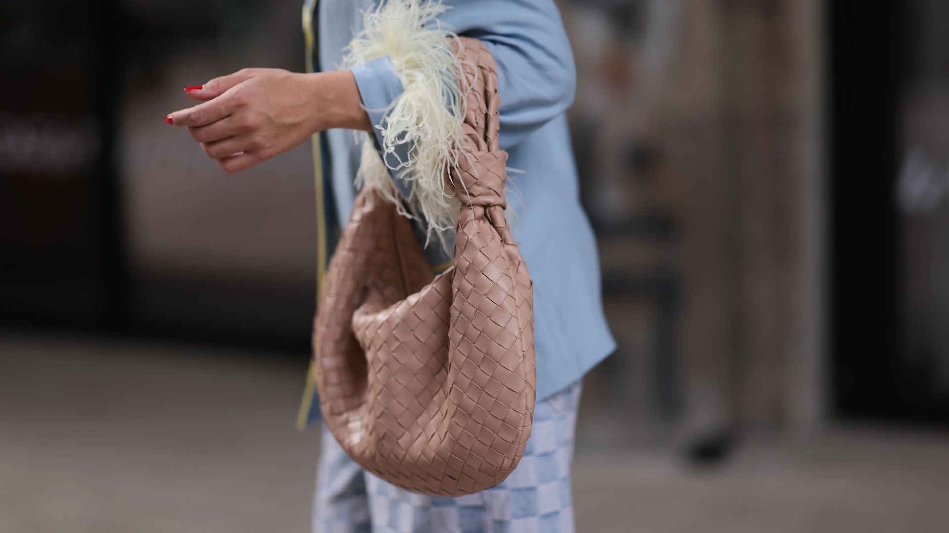 Woman's arm with sleeve showing yellow feathers holding a light brown leather purse. 
