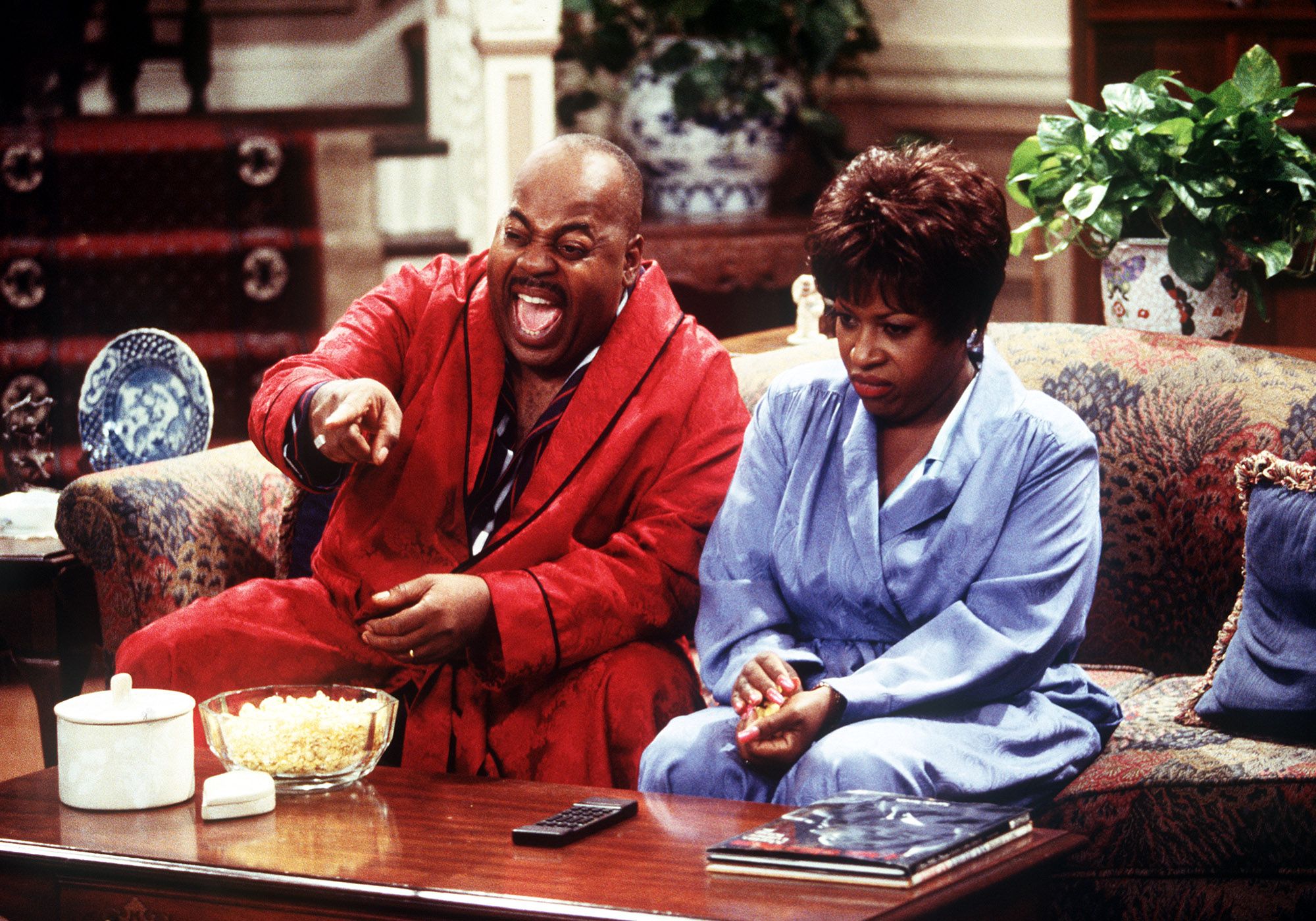 A screenshot from a television show where two people are laughing on a couch. 