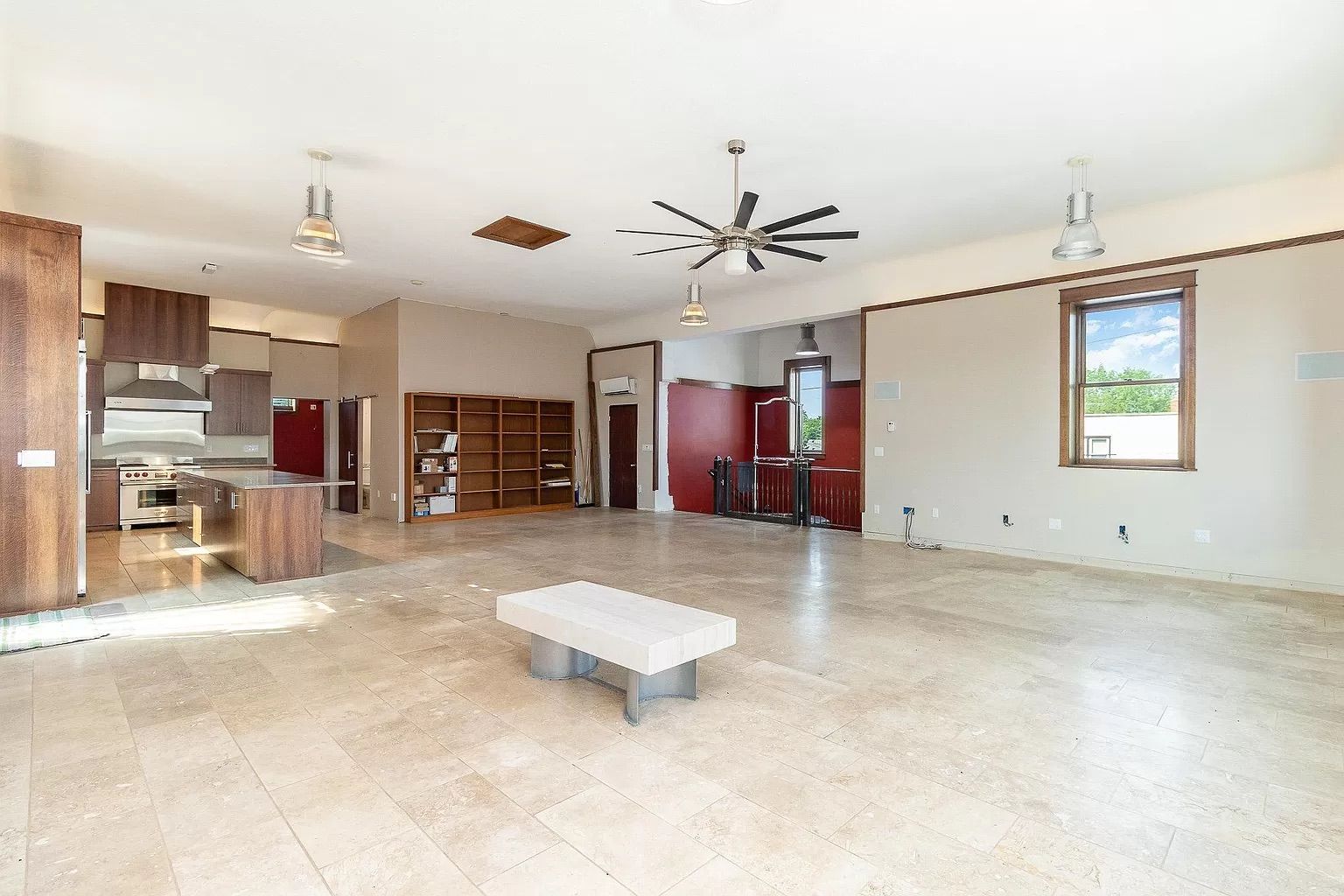 A large empty room with a kitchen and bookshelves visible in the background.