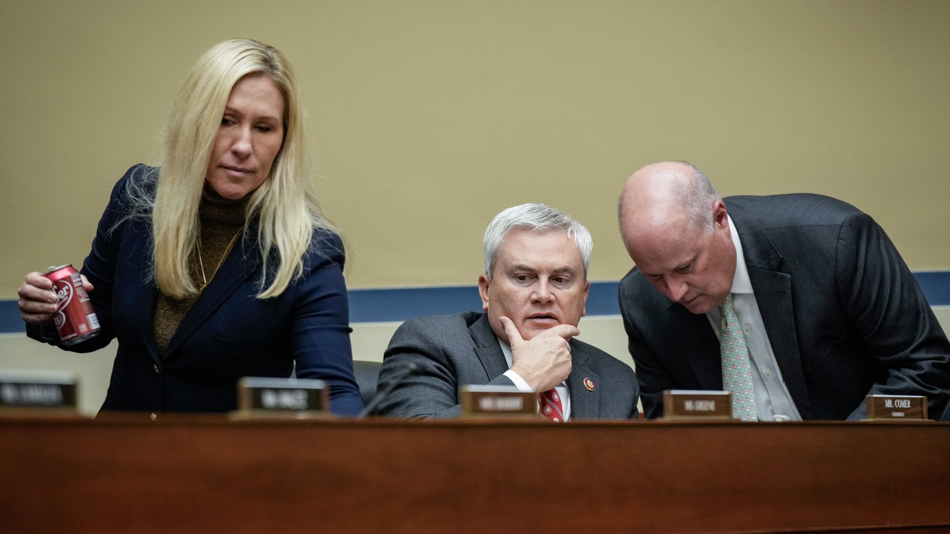 Reps. Marjorie Taylor Greene, wearing a blue jacket and brown turtleneck, and James Comer, wearing a gray suit, sitting at a committee dais.