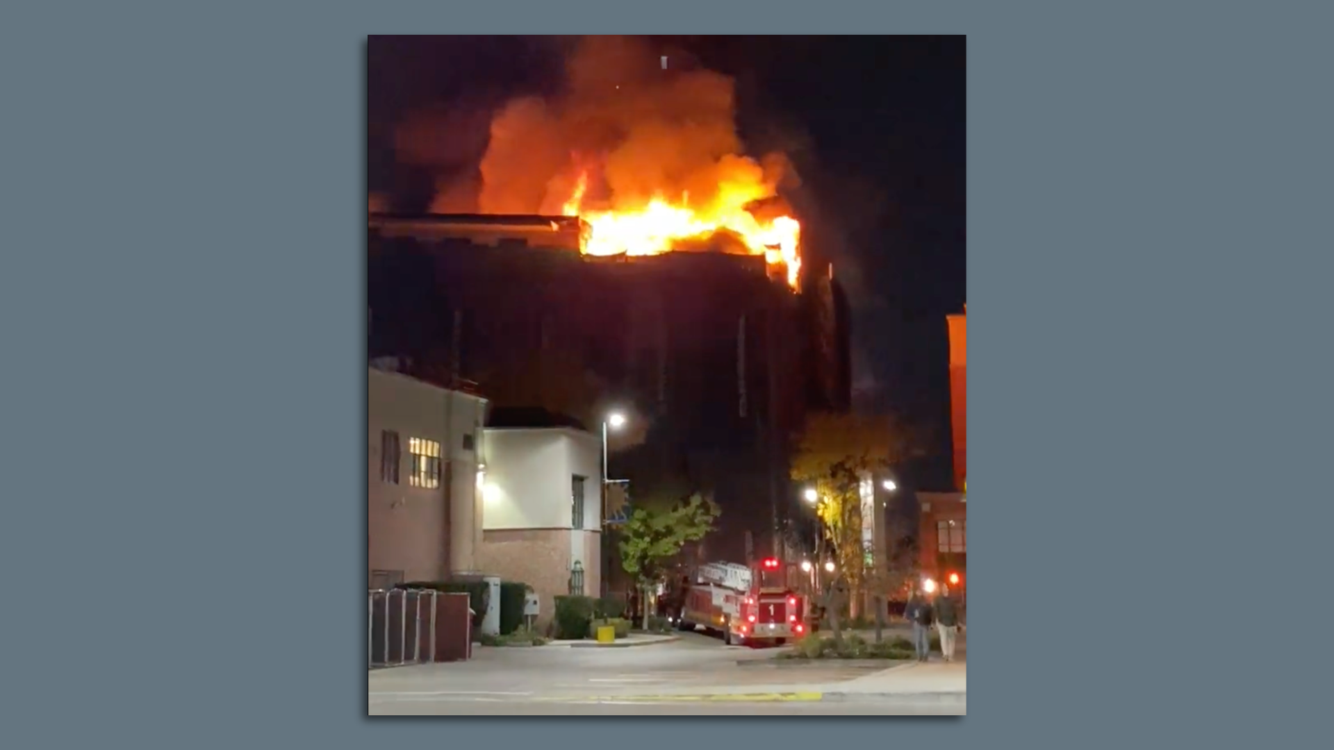 A huge fire burns at night in a large building on a city street with fire trucks.