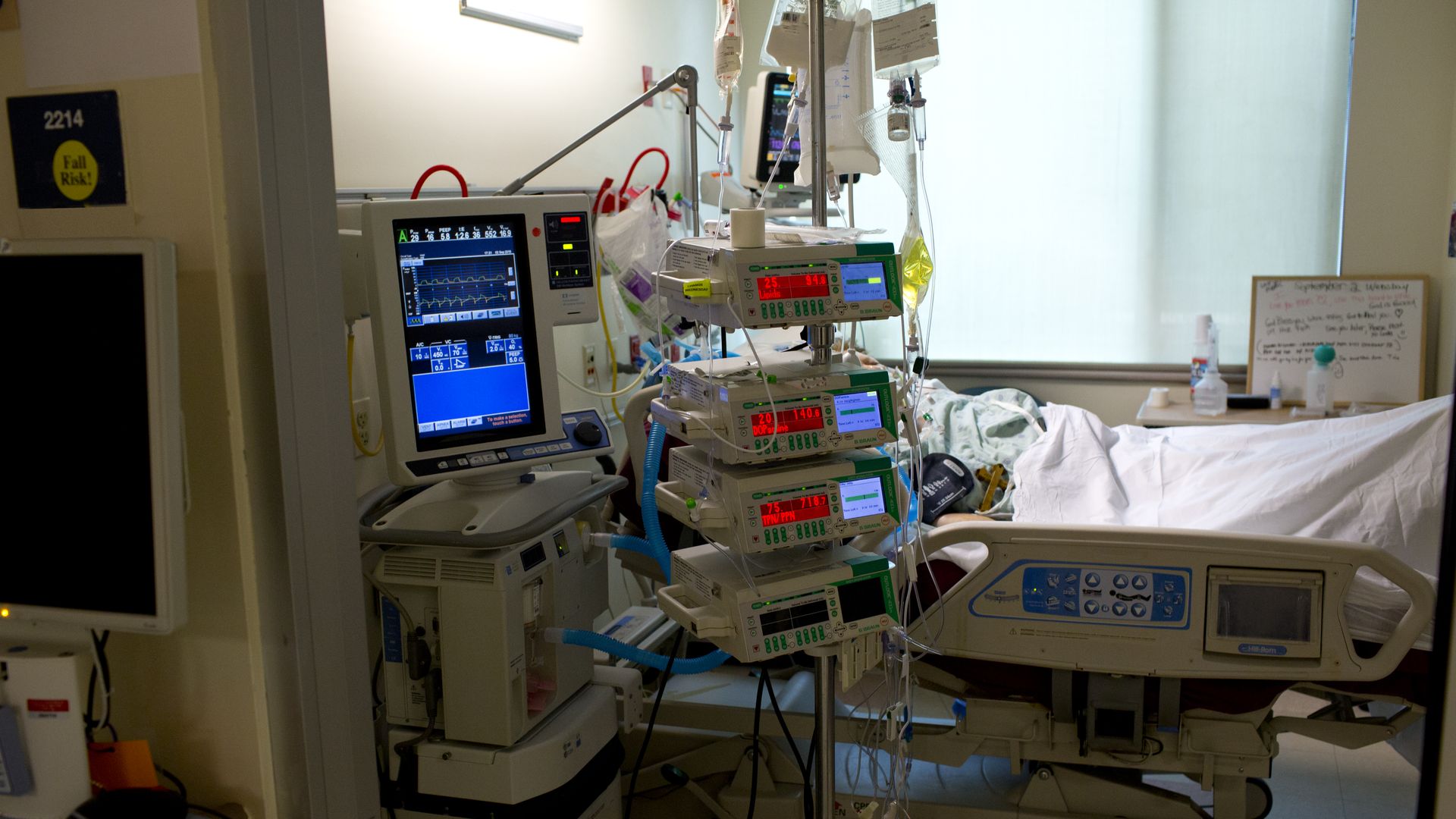 A patient sits in a hospital bed with machines nearby.
