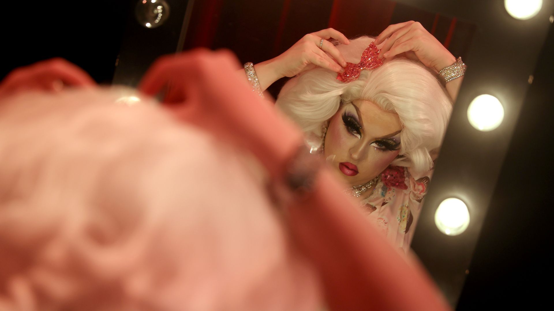 Photo of a drag performer styling herself in a mirror