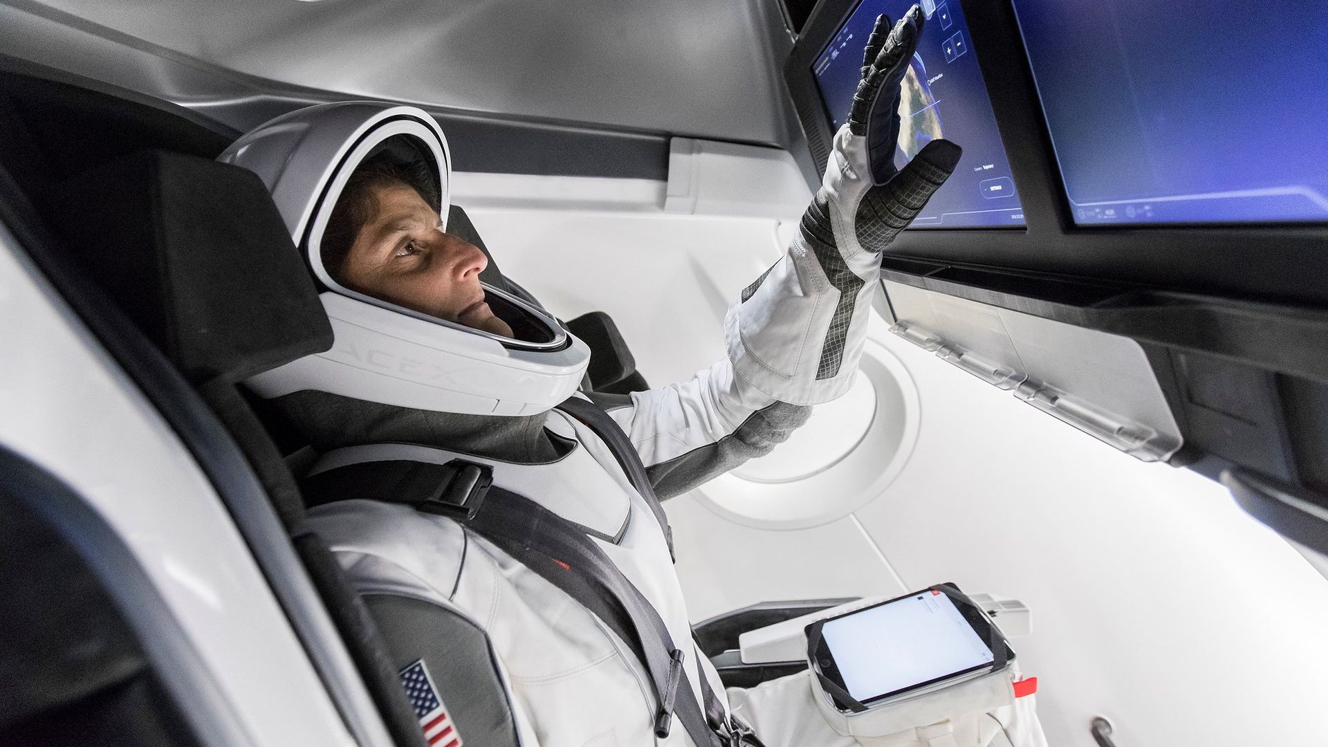 A person in a spacesuit touching a tablet in a space capsule