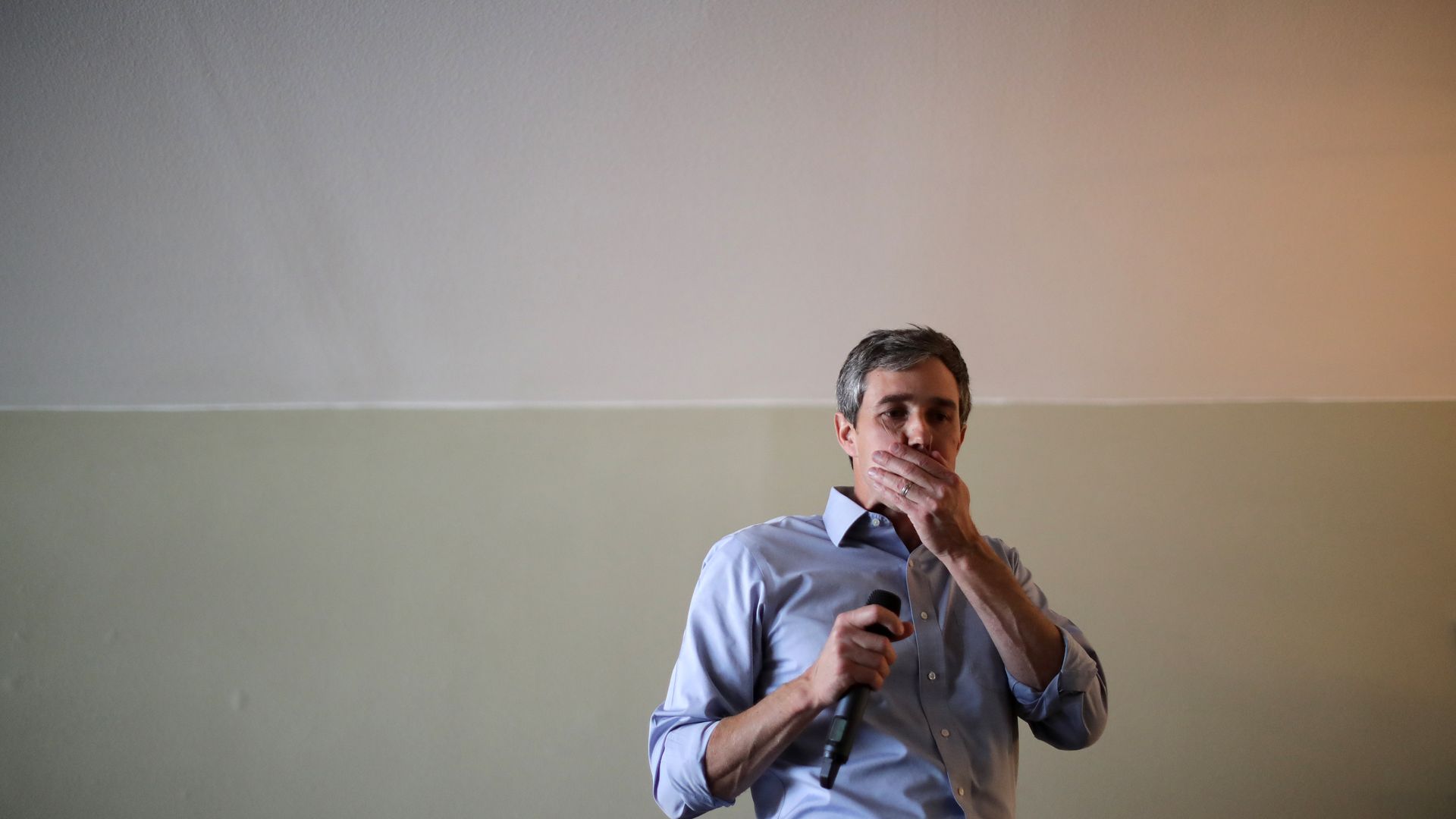 Beto O'Rourke stands and holds his face with a microphone.