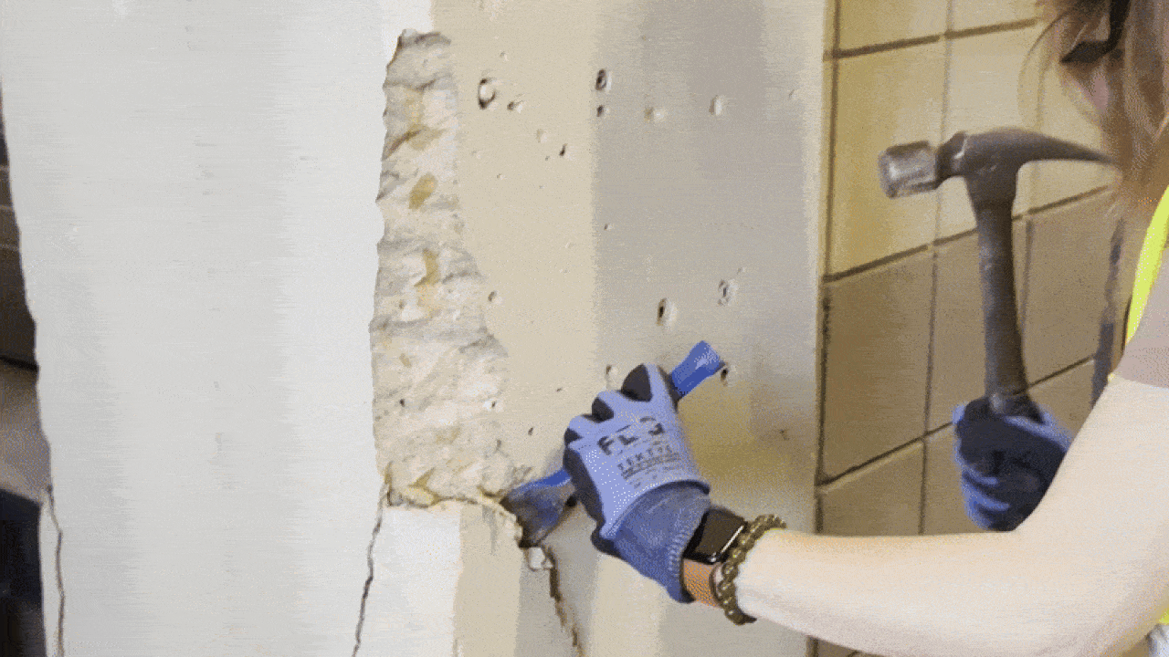Artist Megh Knappenberger wears a hammer and construction vest while hammering a chisel into a concrete pillar at the old KU stadium.