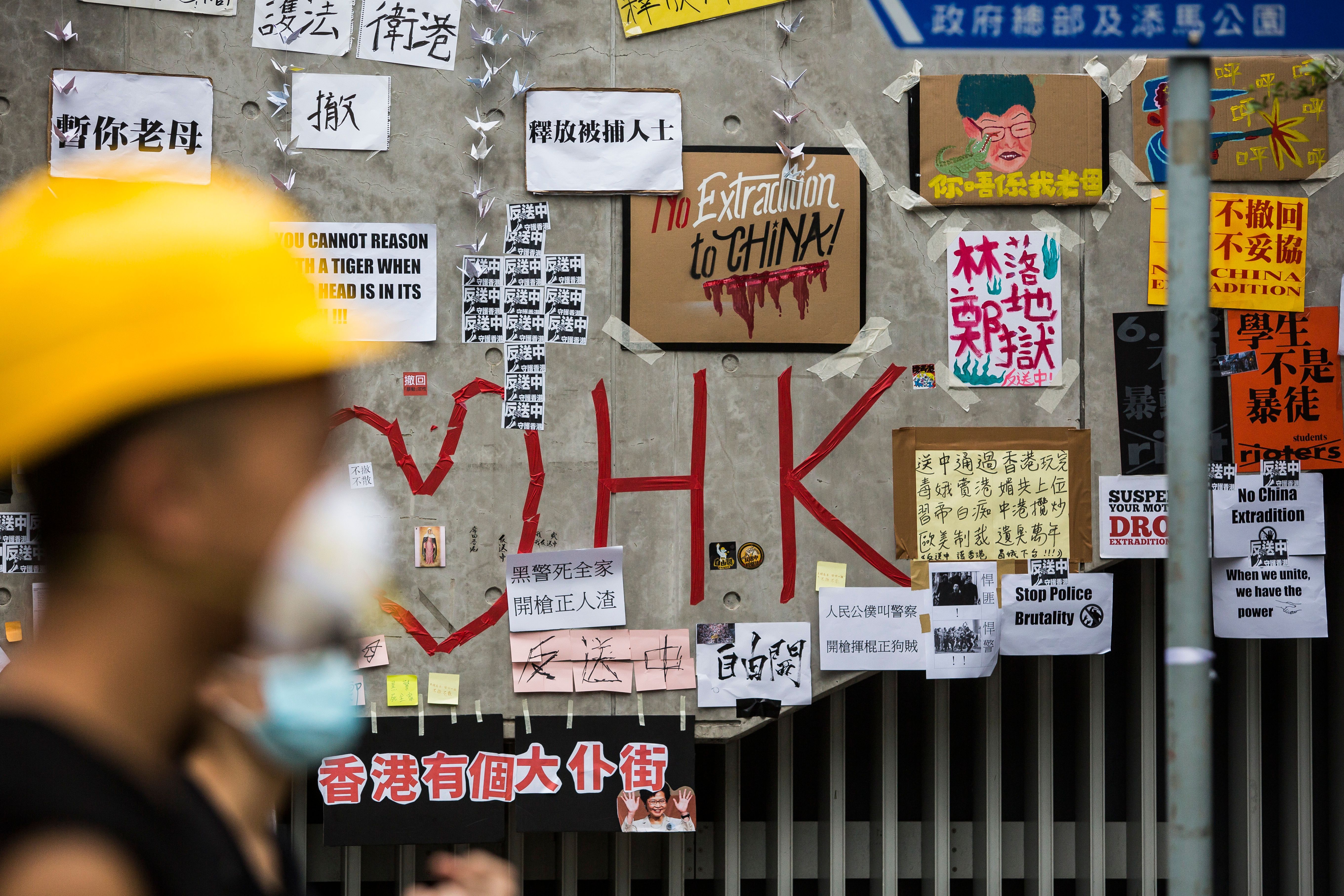 eople walk past a wall covered in messages and posters in Hong Kong early on June 17, 2019. 