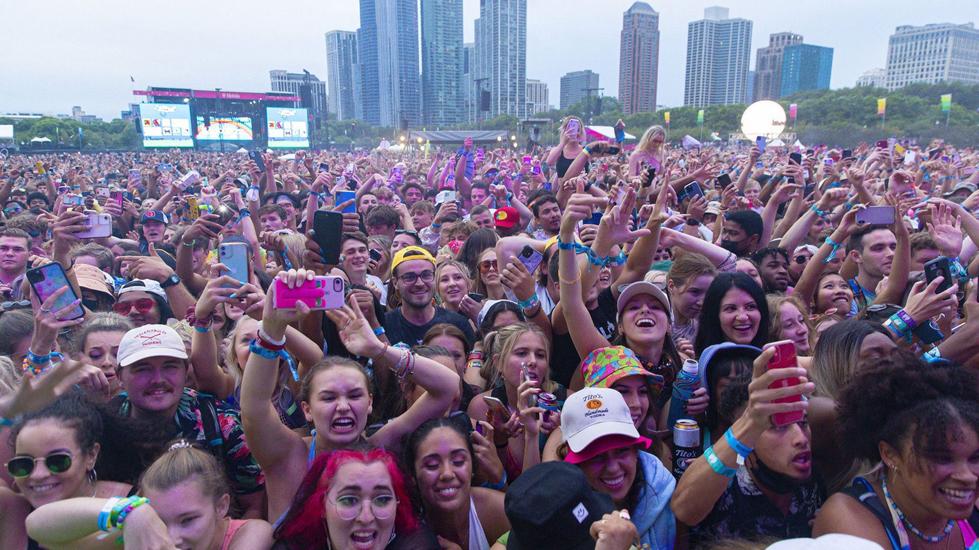 Photo of crowd watching concert with tall buildings in background. 