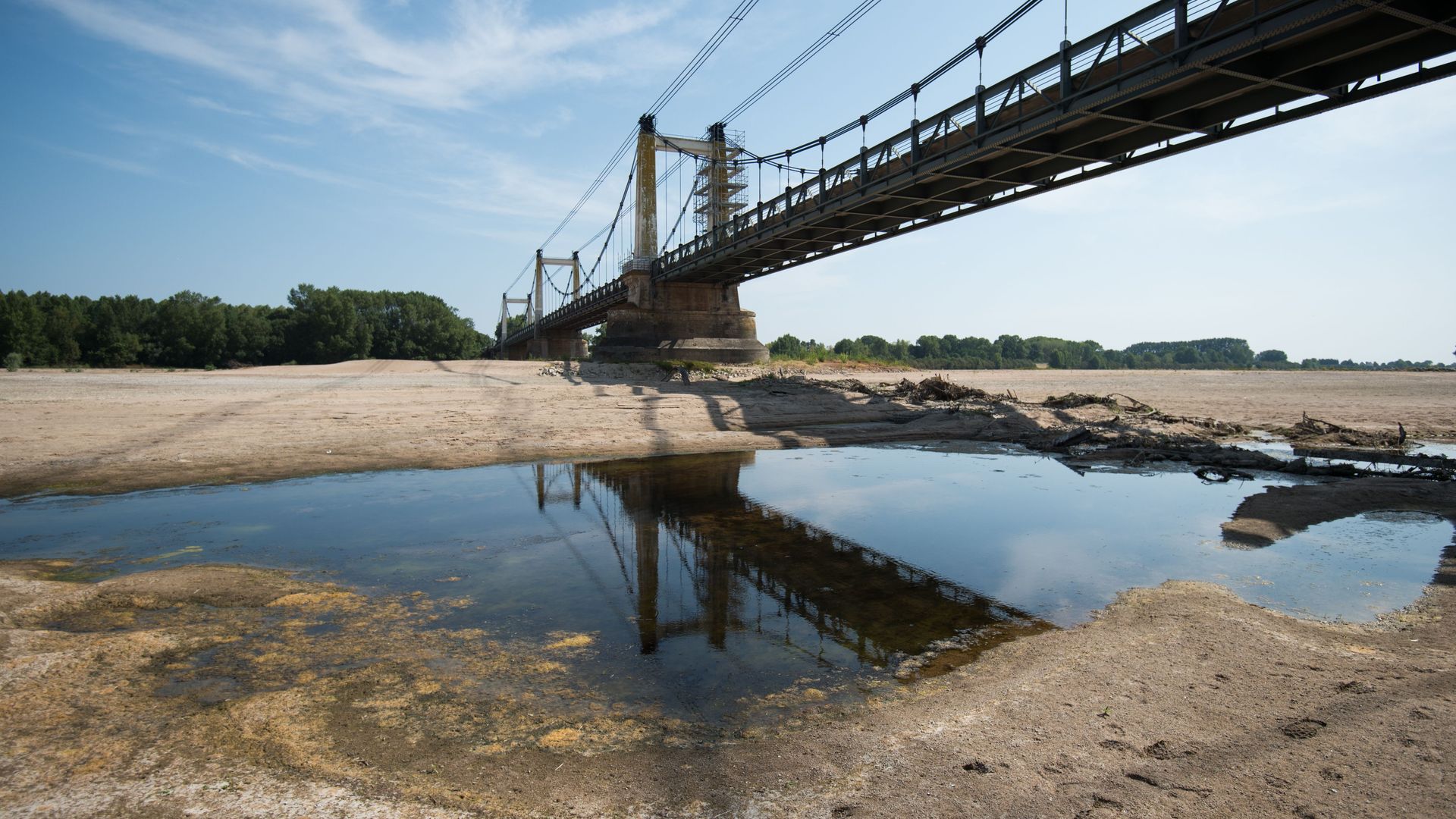 This image shows a mostly dry riverbed with a large bridge over it and trees in the distance