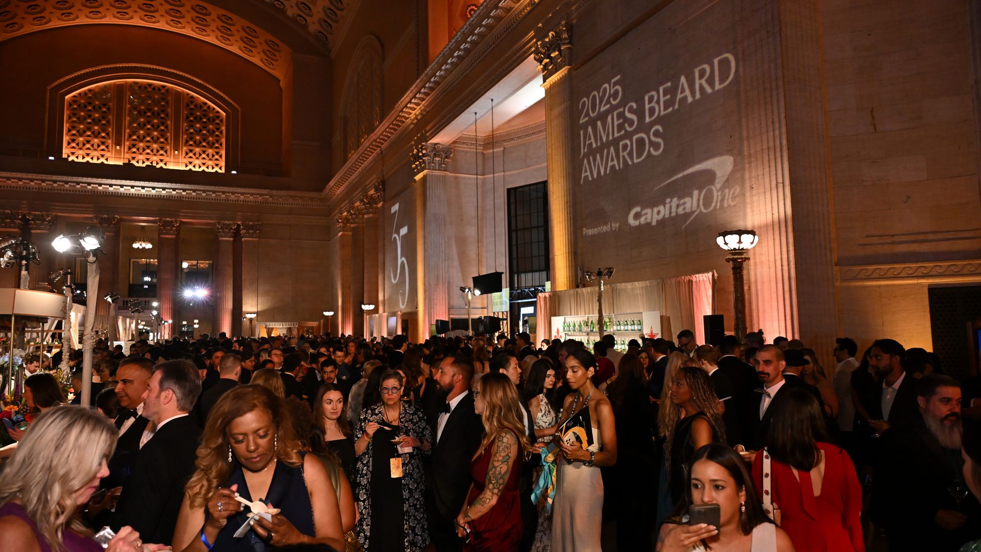 Crowded elegant event inside grand hall with high ceilings and warm lighting, featuring guests in formal attire at the 2025 James Beard Awards presented by Capital One.