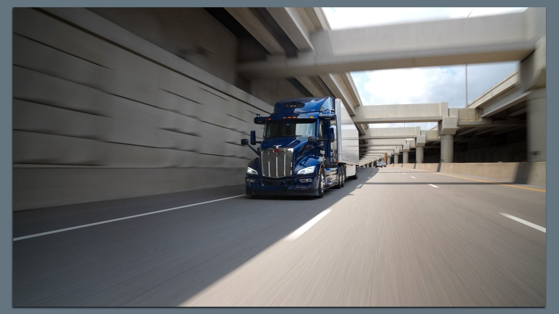 Image of a self-driving Aurora semi truck on a highway alongside a tall concrete wall 
