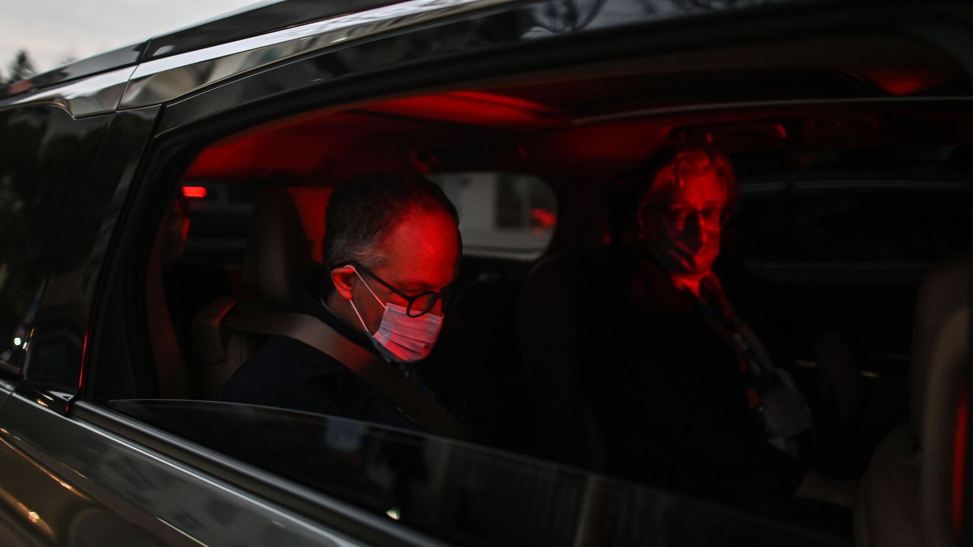 Picture taken from the side of a car with its windows down, two men sit inside of the car, they are two of the members of the WHO team investigating the origin of the coronavirus