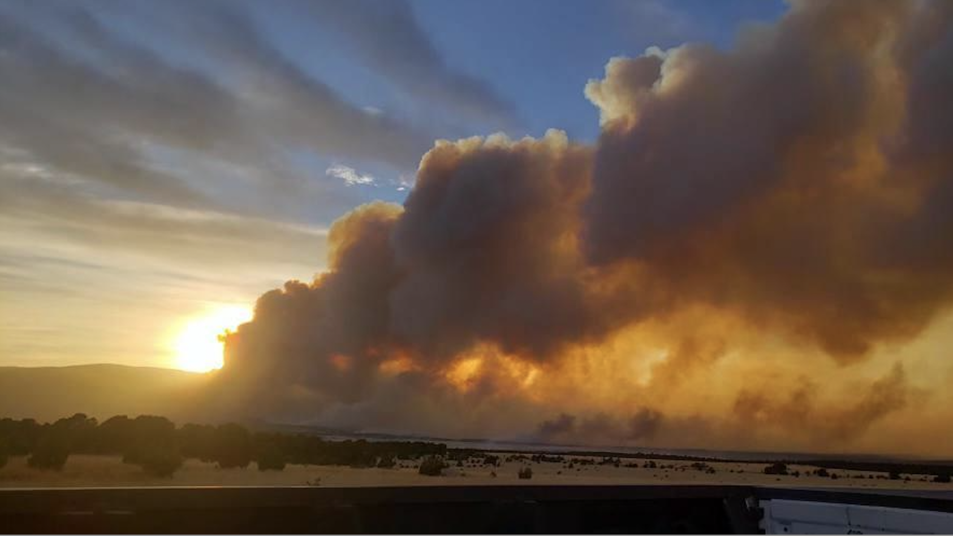 A large plume of smoke is seek from a distance in New Mexico as the sun sets in the background