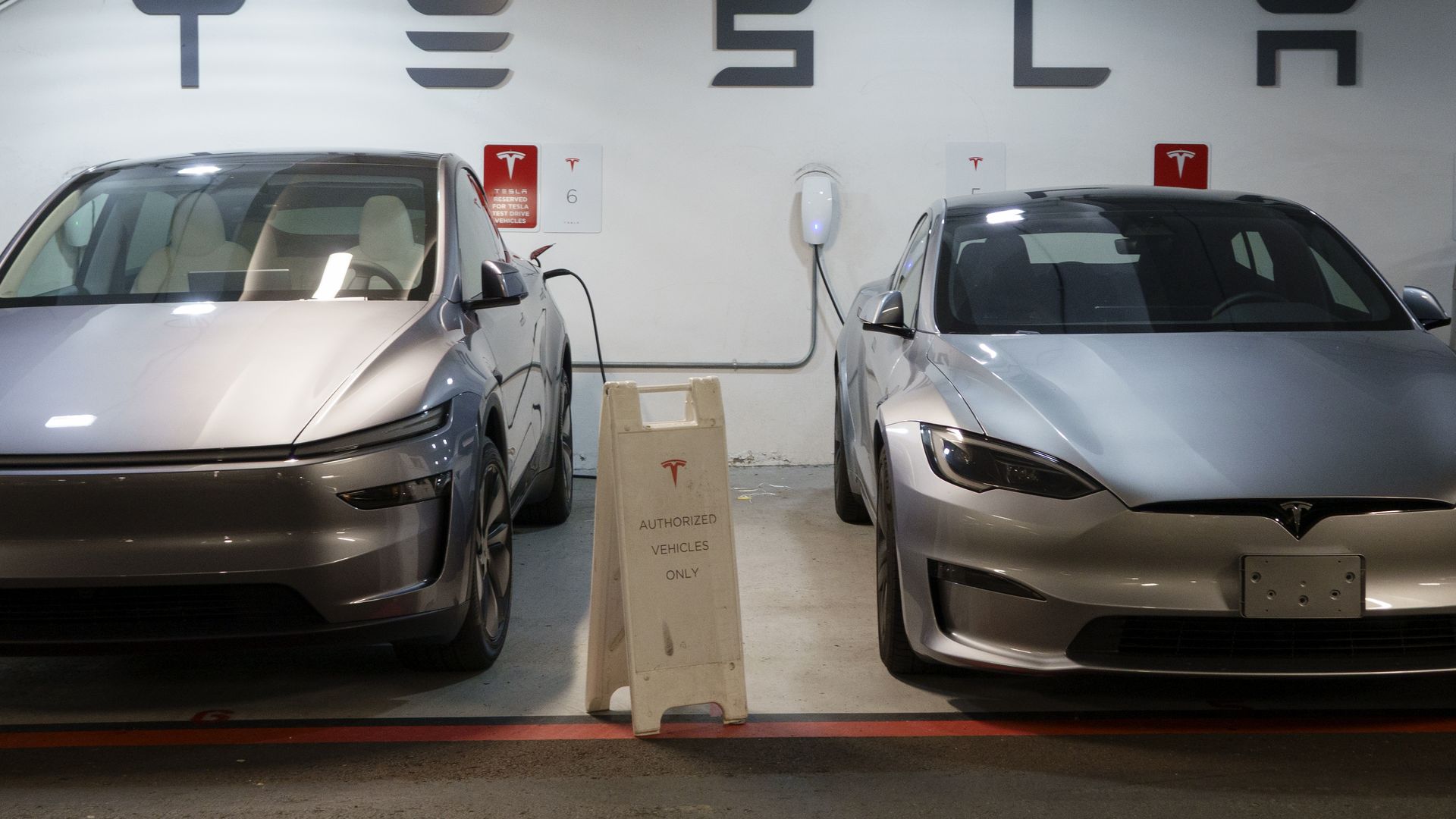 A photos showing two Teslas parked side by side below a sign reading "Tesla."