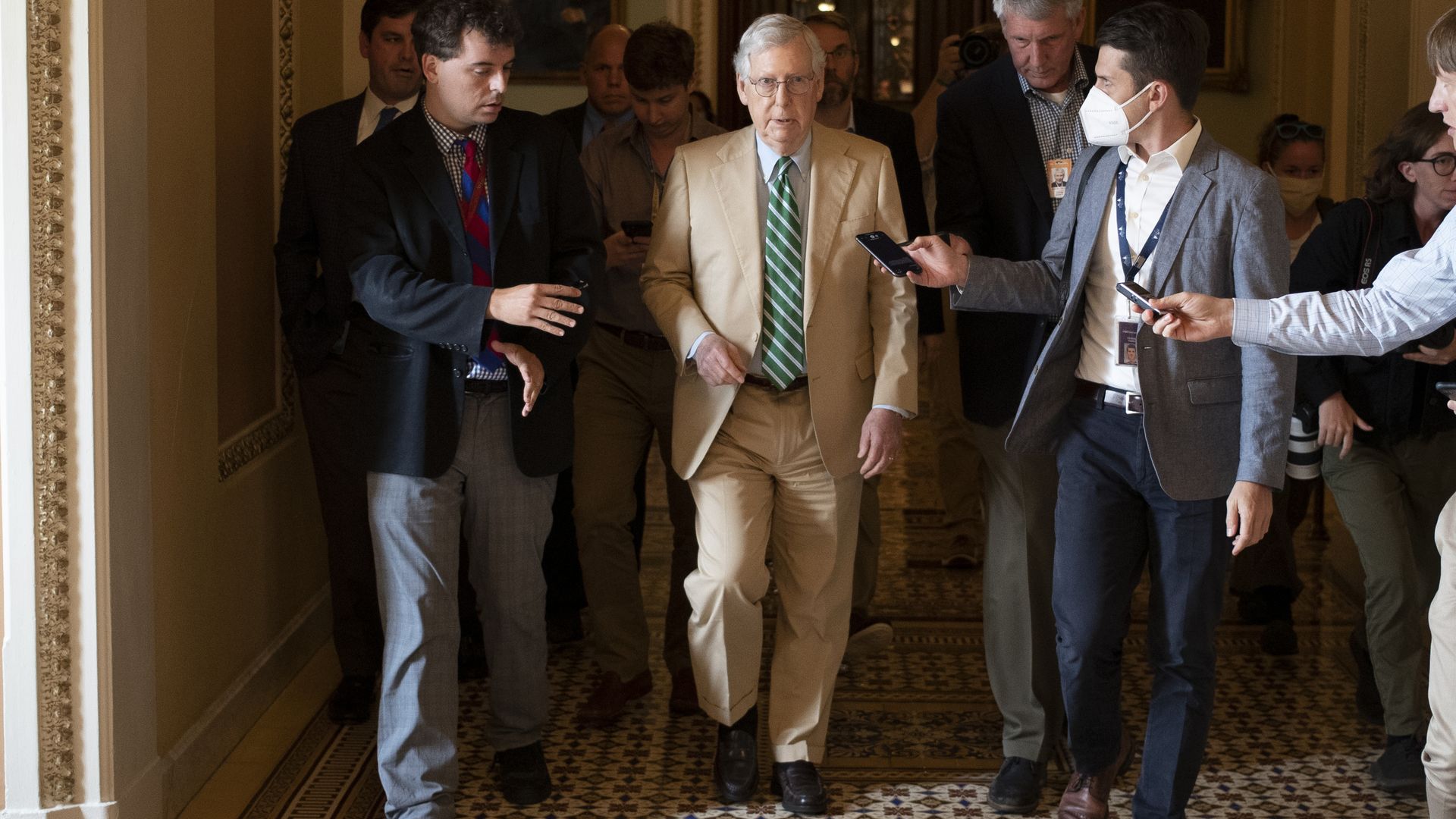 Senate Minority Leader Mitch McConnell is seen speaking with reporters as he walks down a Capitol hallway.
