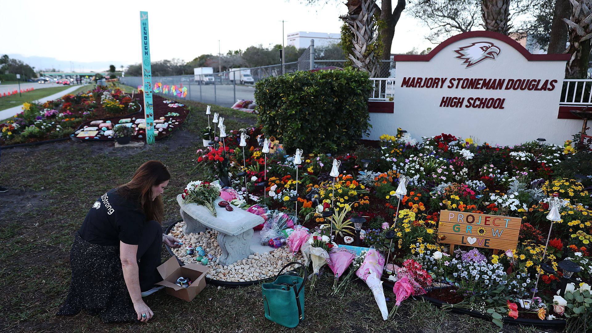 This image shows a large memorial of flowers and plaques underneath the Stoneman Douglas High School welcome sign.