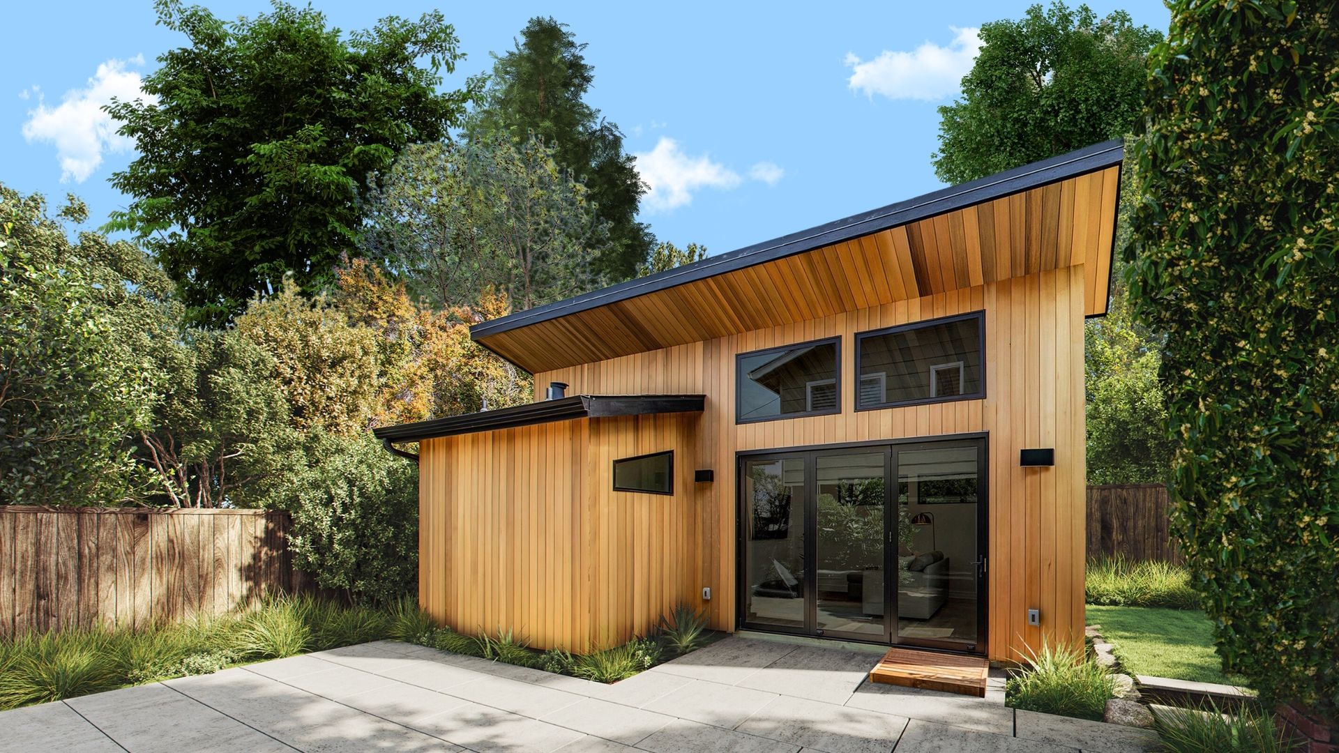 An accessory dwelling unit with wood siding is shown surrounded by trees, with a paved area in front of it. 