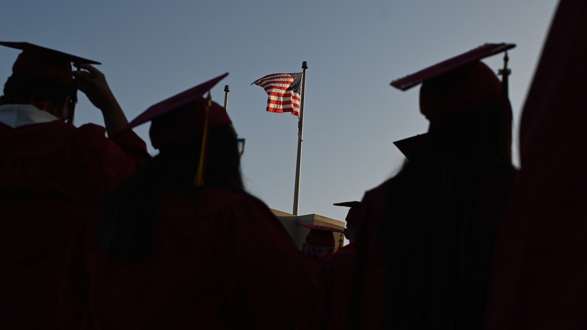 Students at a graduation ceremony with the American flag in the background.
