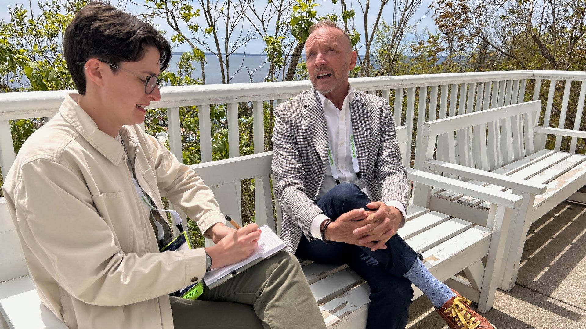 Two people sit talking on a white bench.