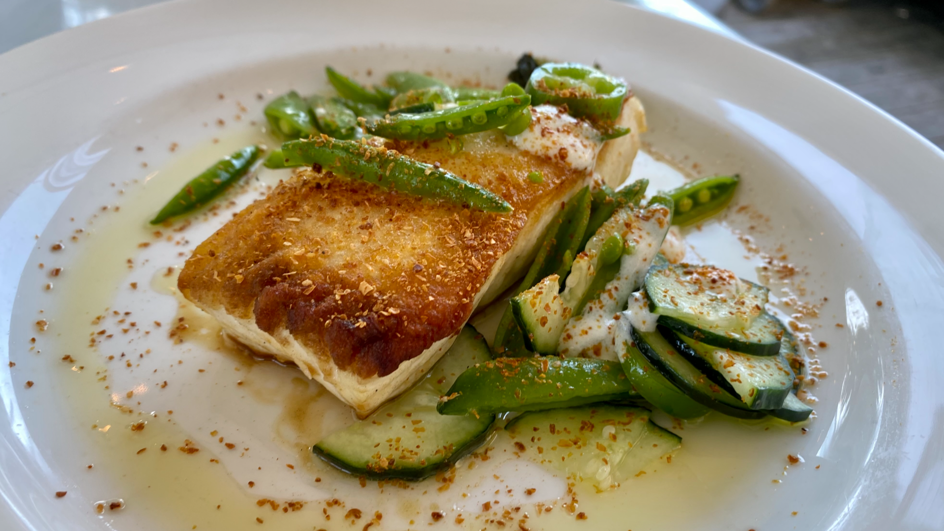 Halibut resting on a bed of vegetables with a sauce on a white plate.