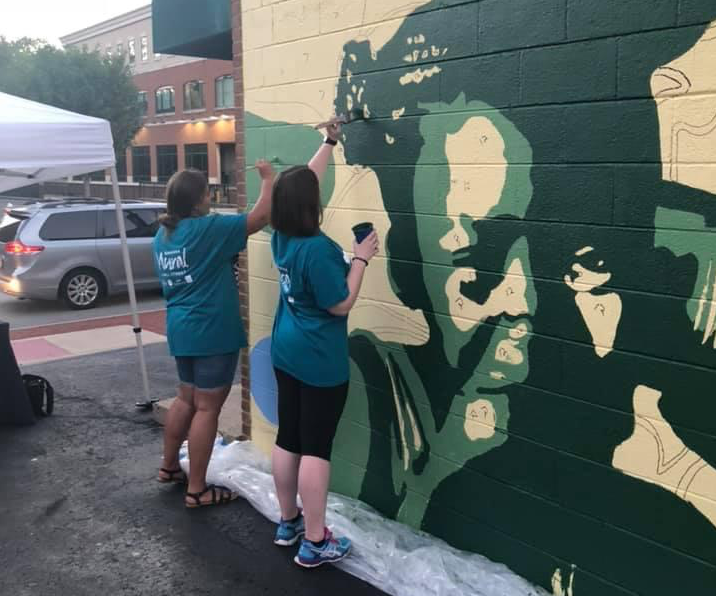A view from behind two people painting the mural
