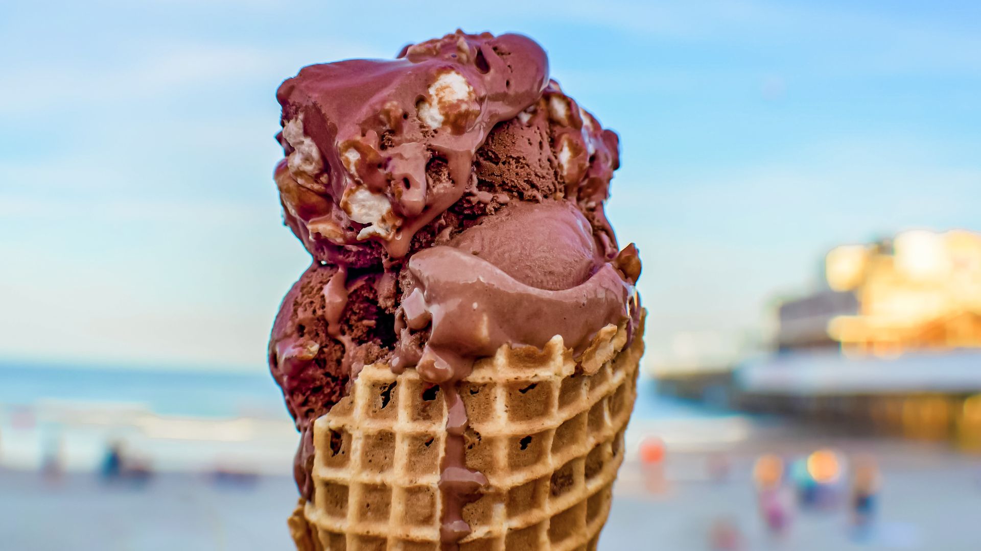 Photo of a Rocky Road ice cream scoop sitting in a waffle cone. It's held against the backdrop of a beach.