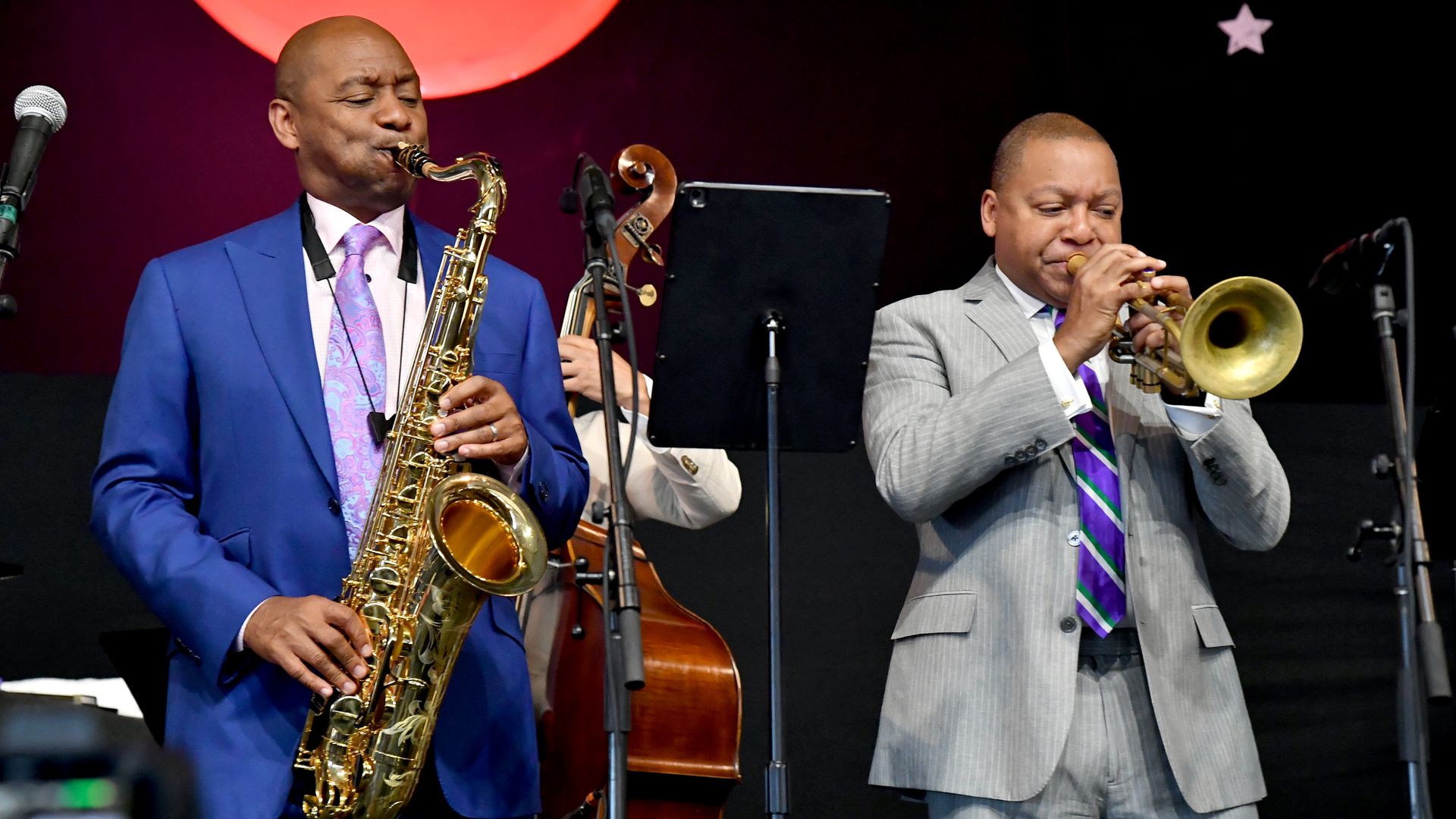 Branford Marsalis plays the saxophone and Wynton Marsalis, at his right, plays the trumpet during an on-stage performance.