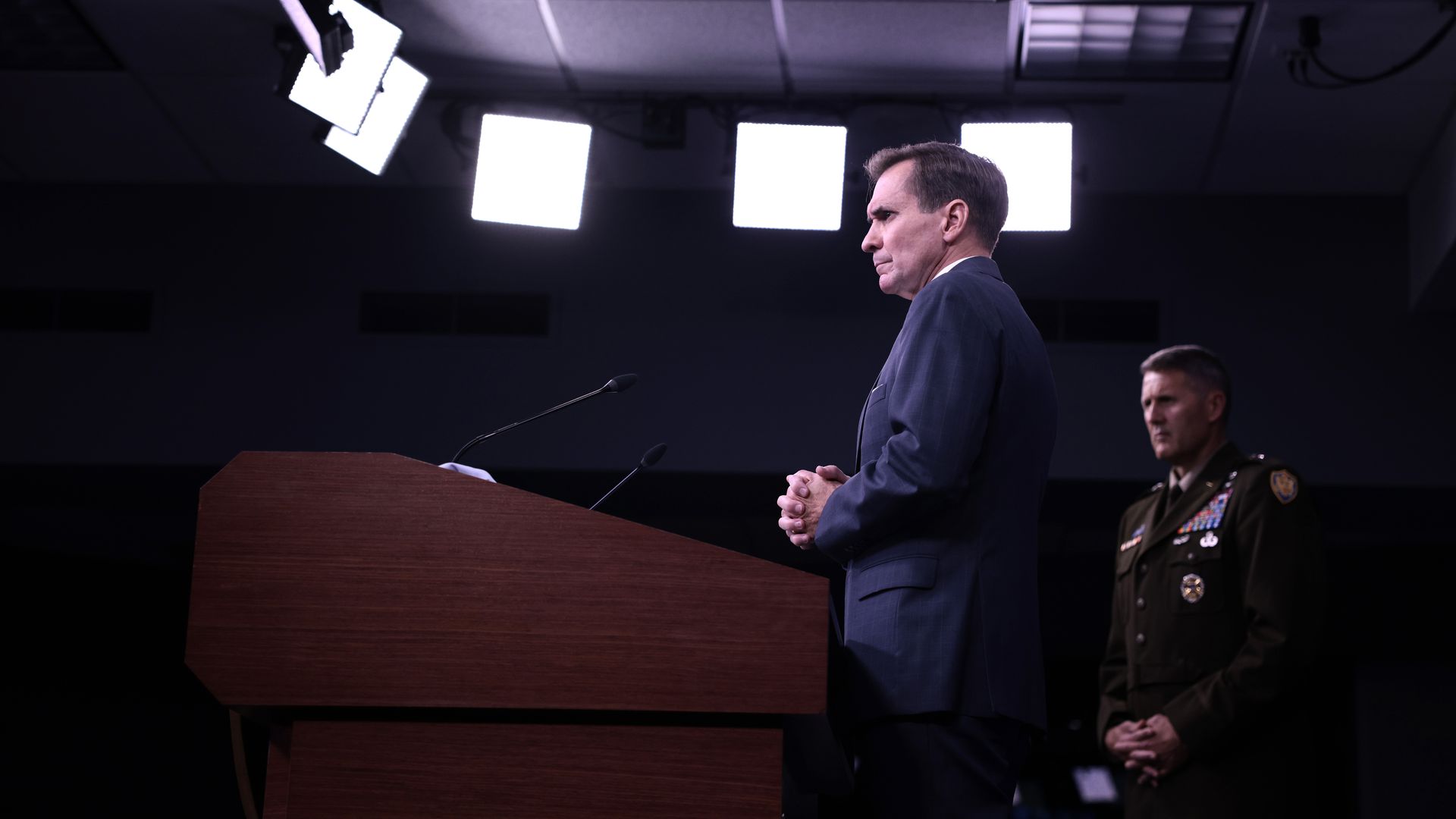 Photo of John Kirby and William Taylor standing at a podium with their hands clasped