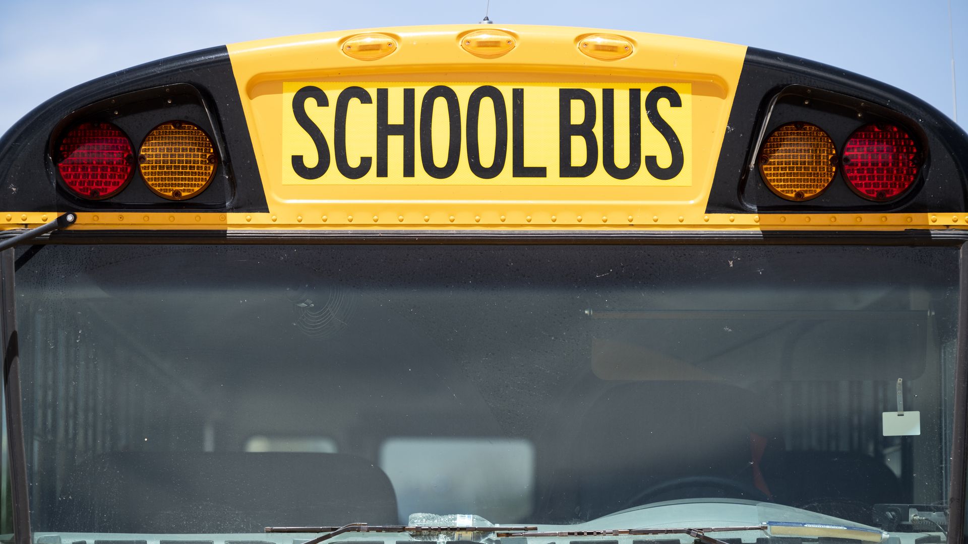 The front of a school bus, with a focus on the words "school bus" above the windshield