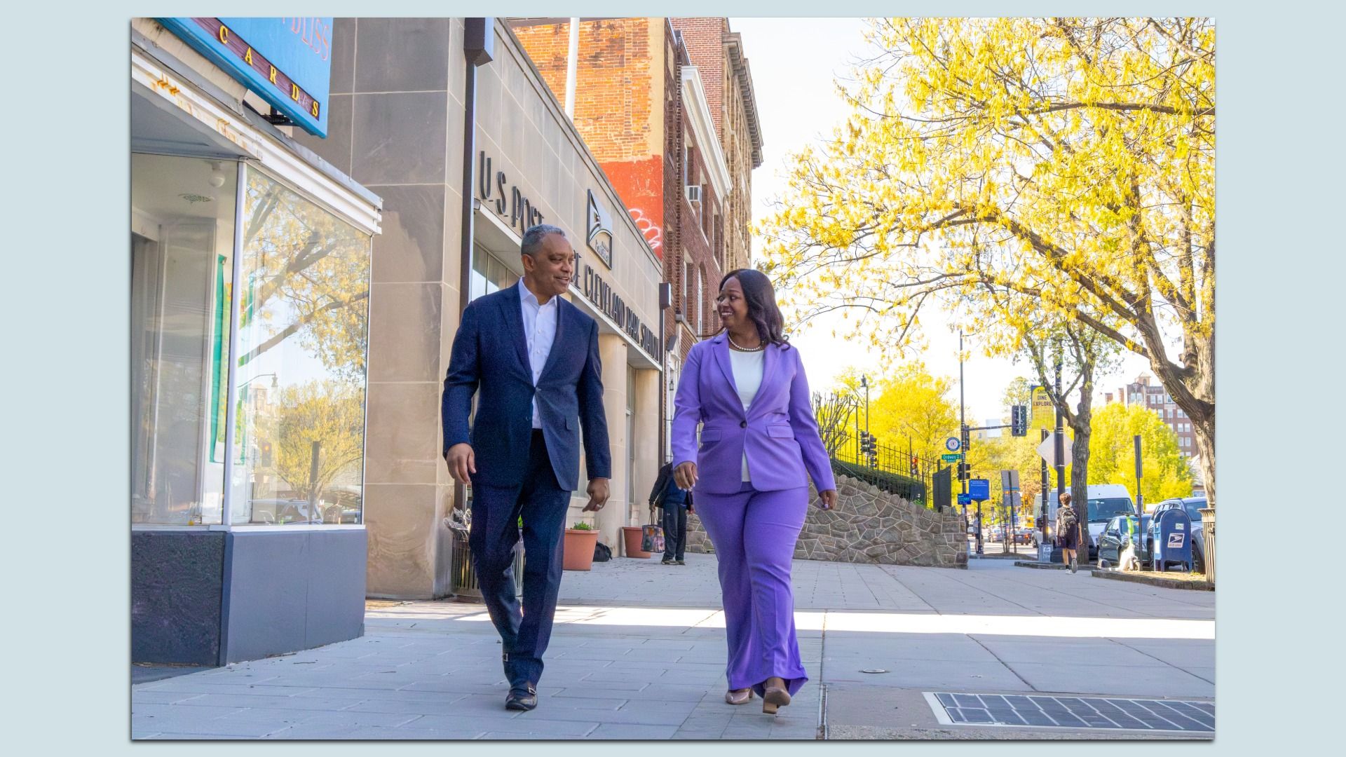 Karl Racine and Janeese Lewis George stroll down a city sidewalk, smiling at each other.