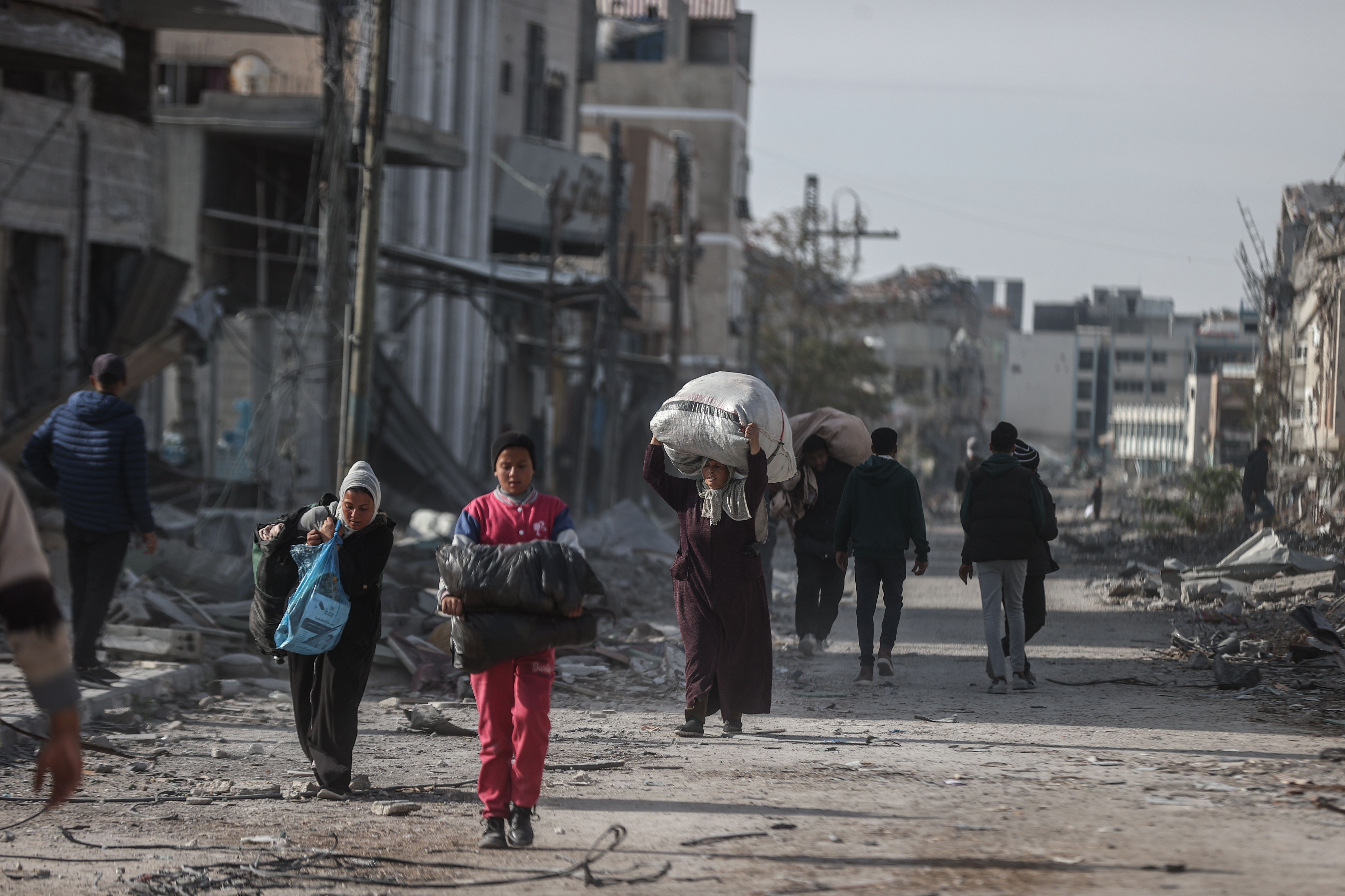 People walk through city ruins with bundles of their belongings
