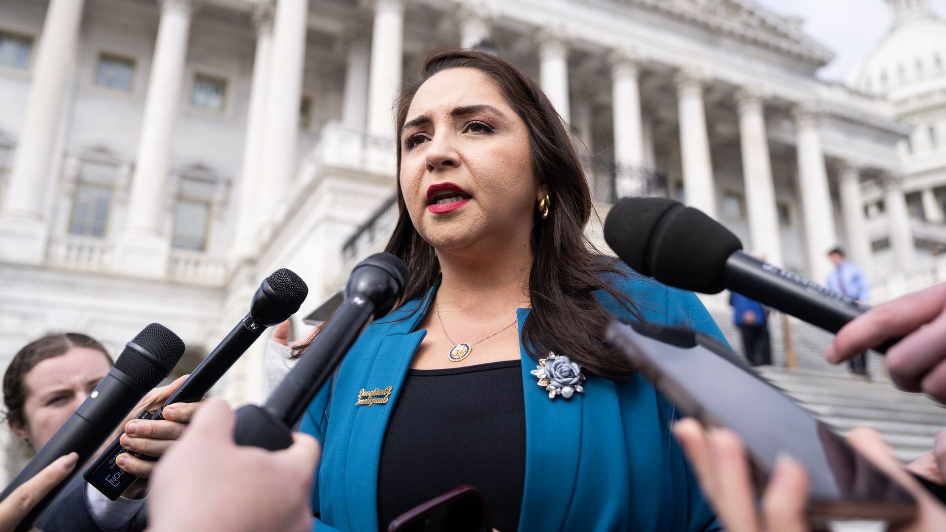 Rep. Delia Ramirez, speaking into microphones while wearing a teal suit outside the U.S. Capitol.
