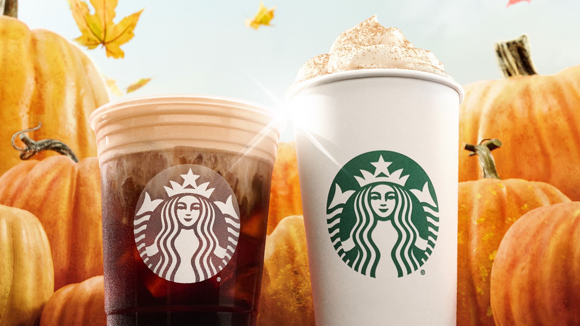 Starbucks cups in front of pumpkins with leaves in the sky